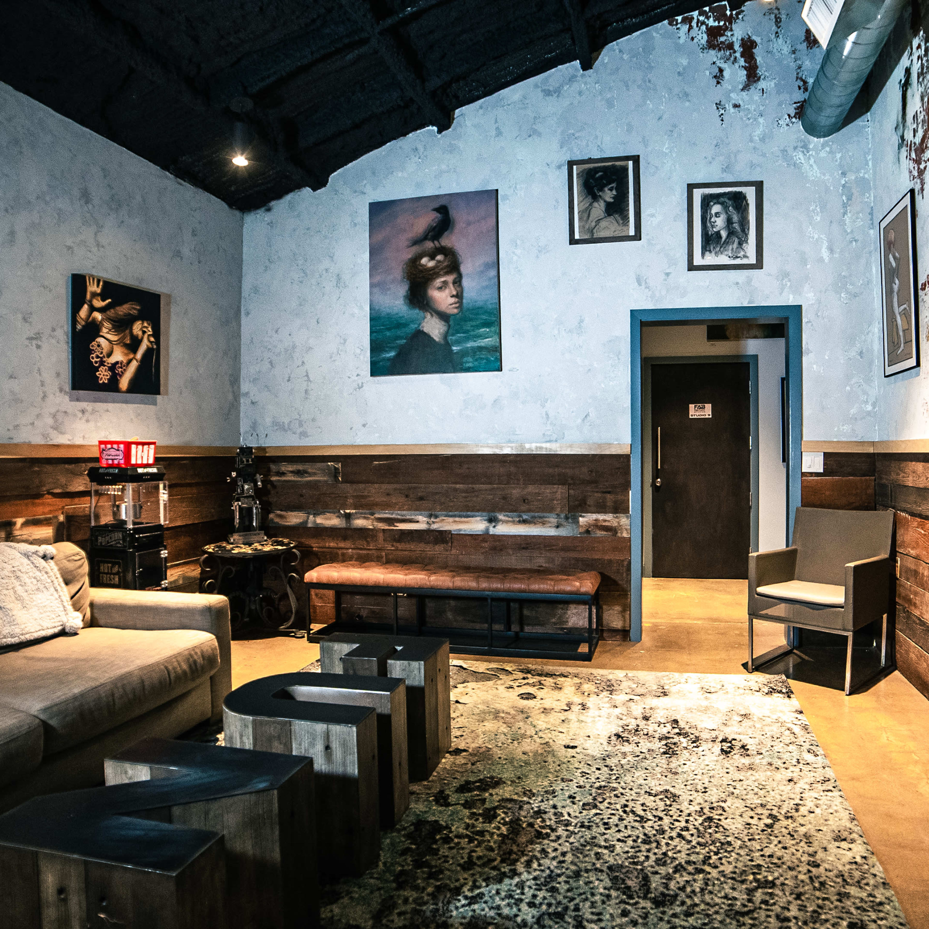 A cozy lounge area with a sectional couch, wooden accents, and several artworks on the walls.