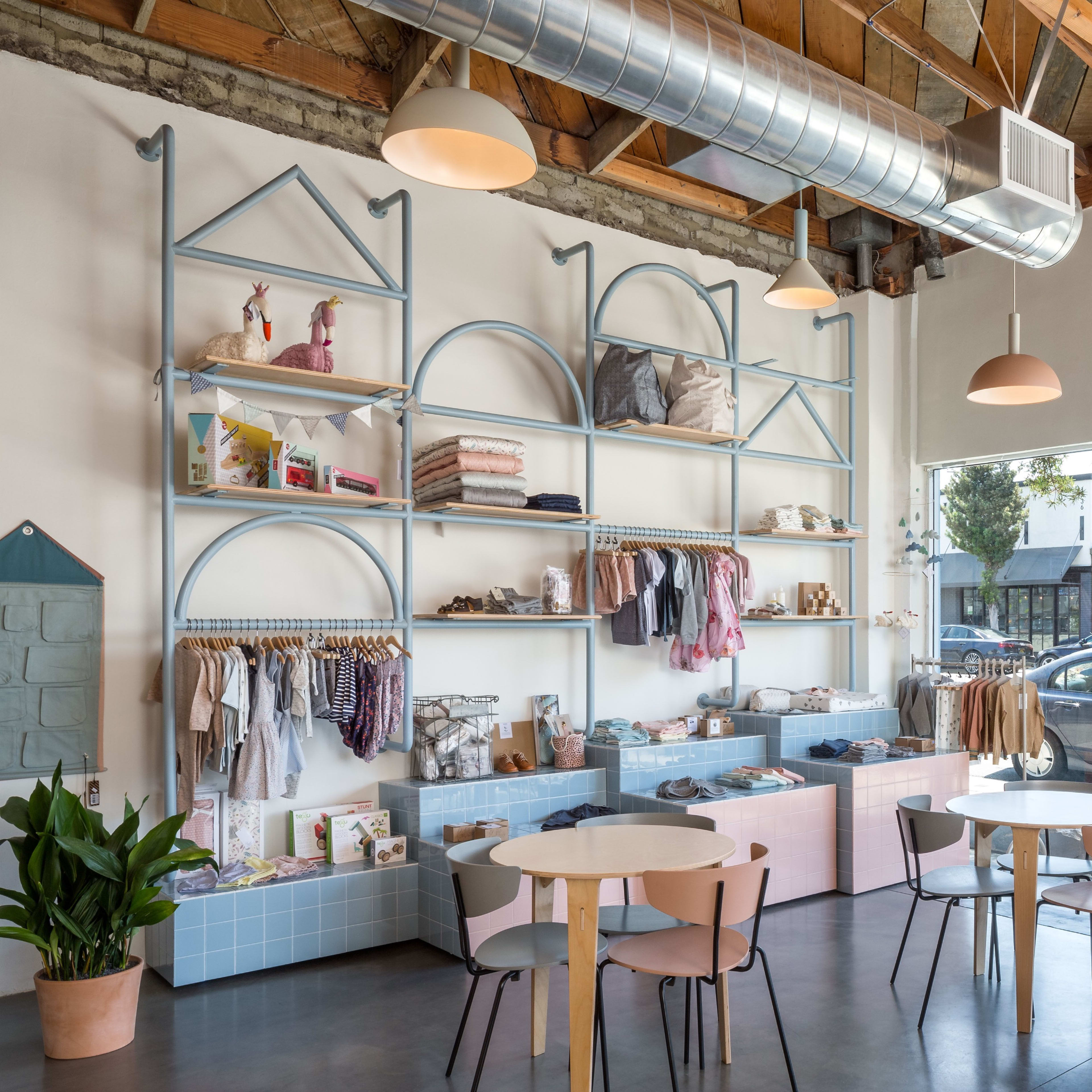 A modern retail space features colorful shelving displaying clothing and accessories, with circular tables and chairs arranged for customer seating.