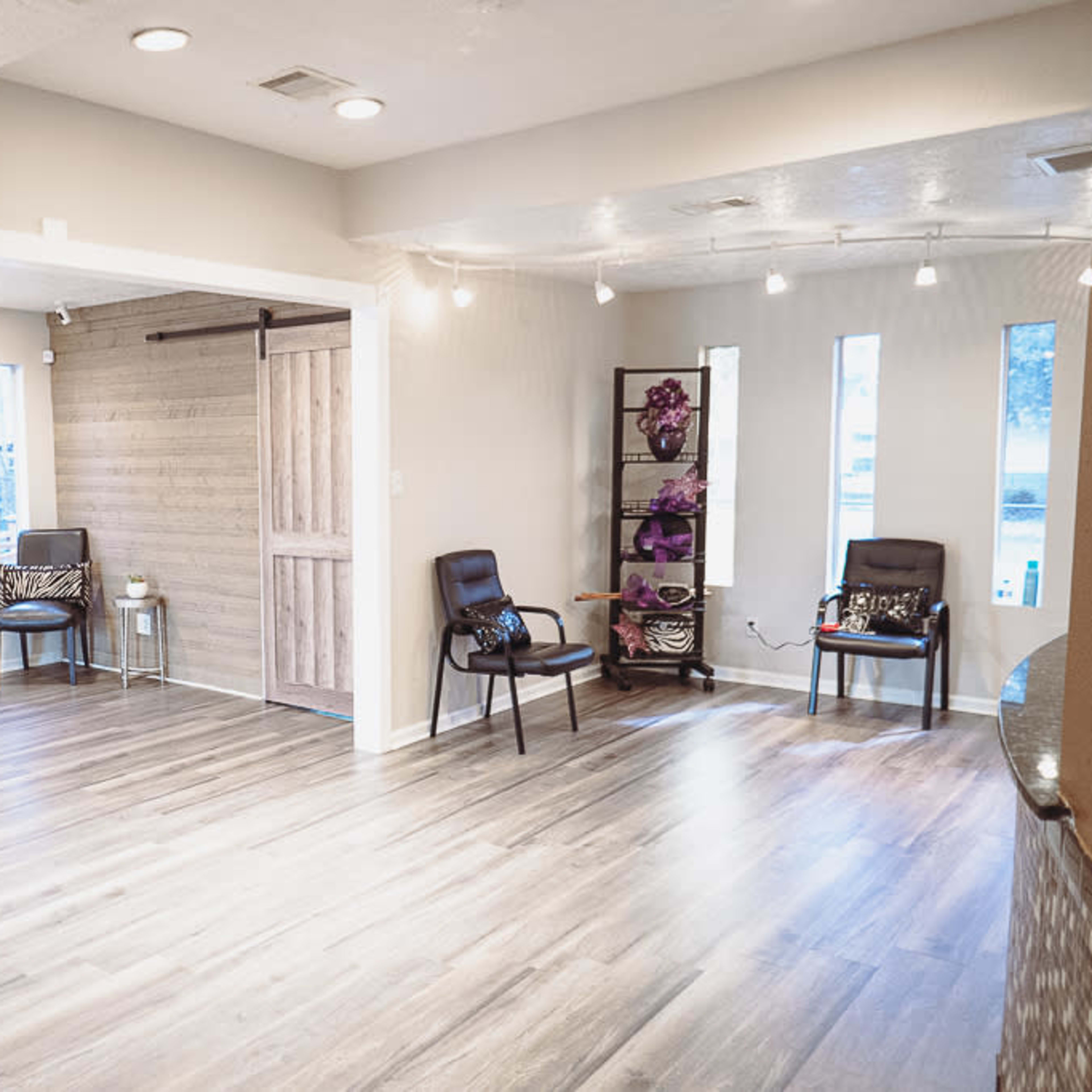 A spacious room with light wooden flooring, featuring two chairs, decorative wall elements, and a sliding barn door.