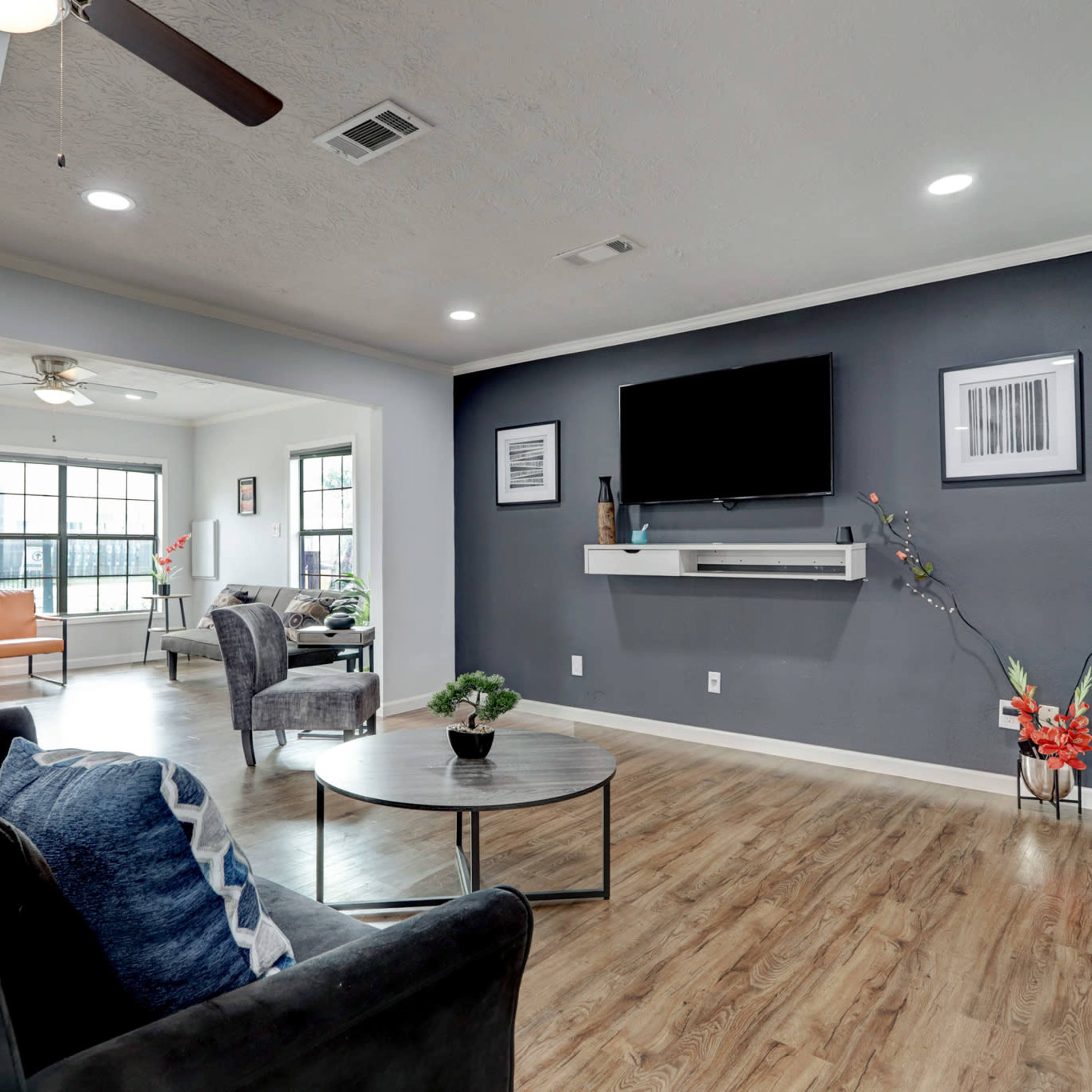 A living room featuring a dark grey accent wall, a wall-mounted television, a coffee table, and seating arrangements including a black sofa and armchairs.