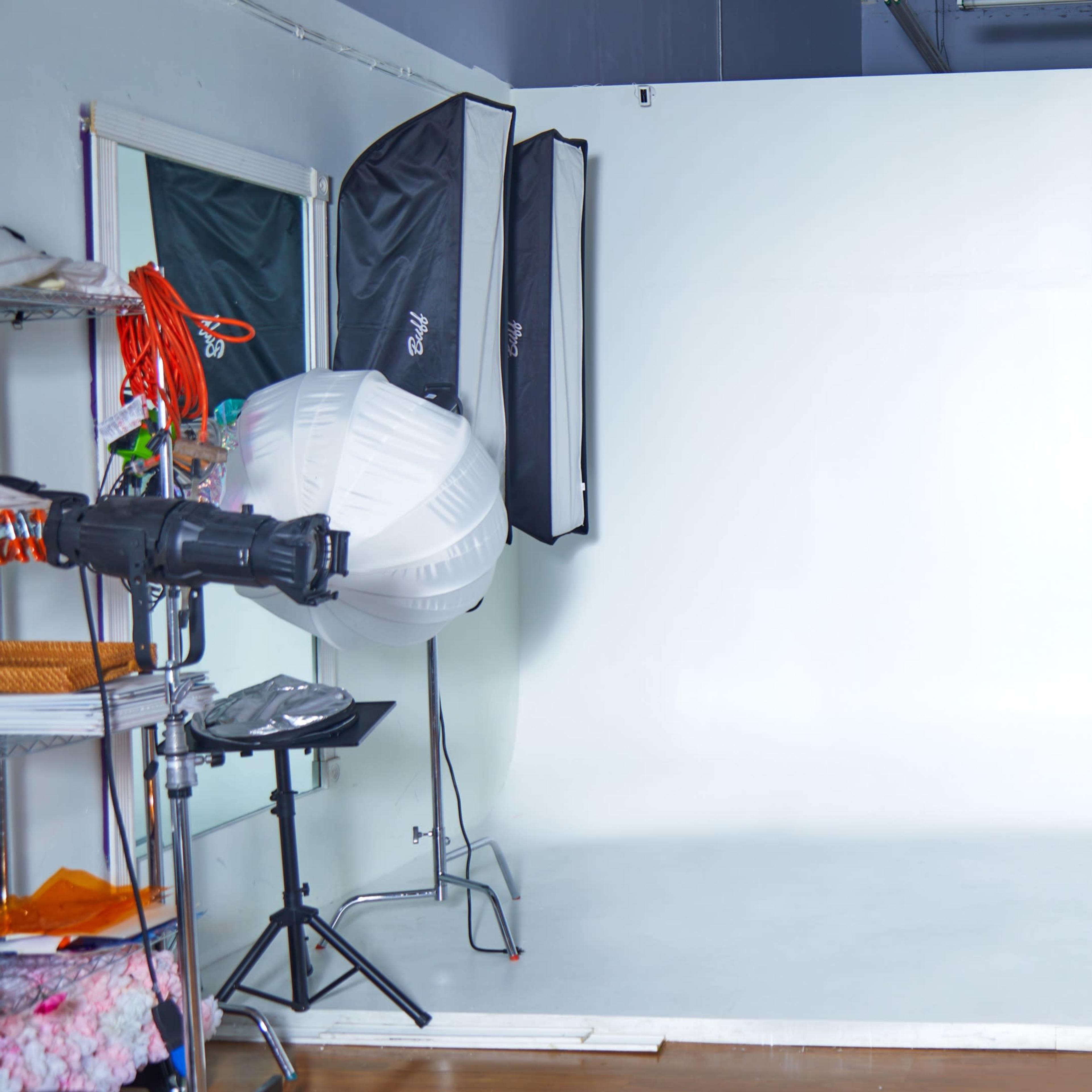 A photography studio features a white backdrop flanked by lighting equipment and a mobile cart.