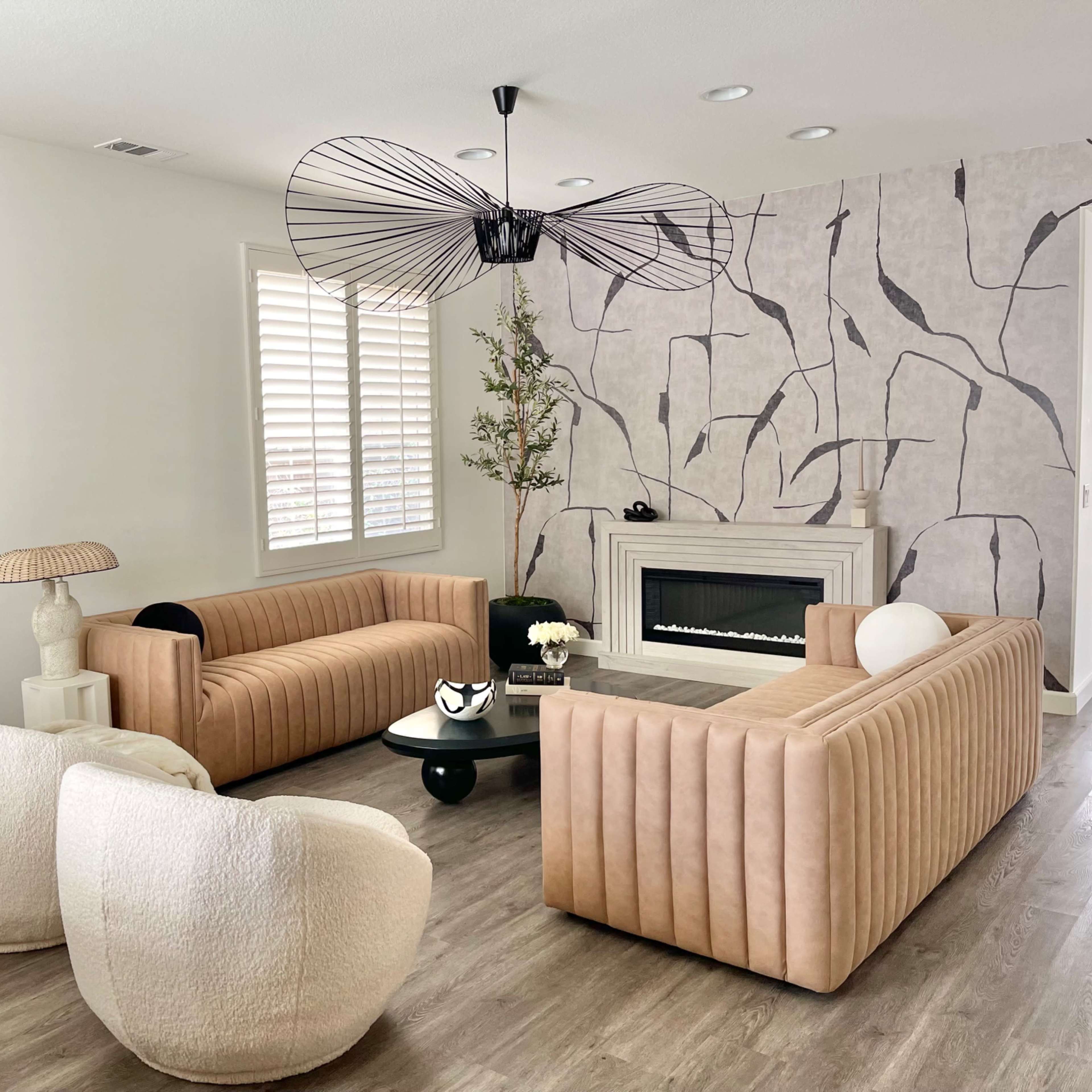 The living room features two beige sofas, a round coffee table, and a fireplace, with a modern light fixture overhead and minimalist decor accents.