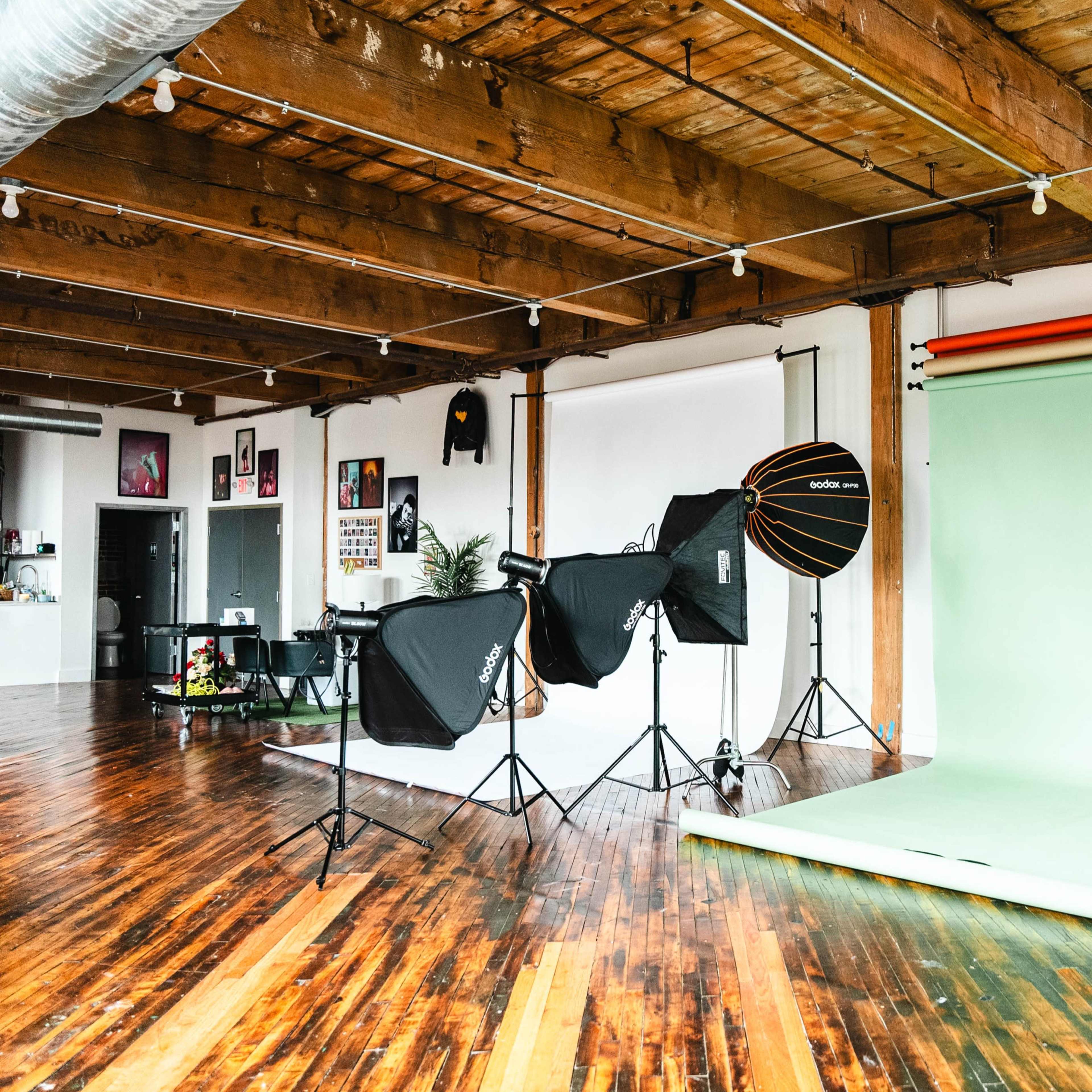 A photography studio featuring a green backdrop, lighting equipment, and wooden flooring.