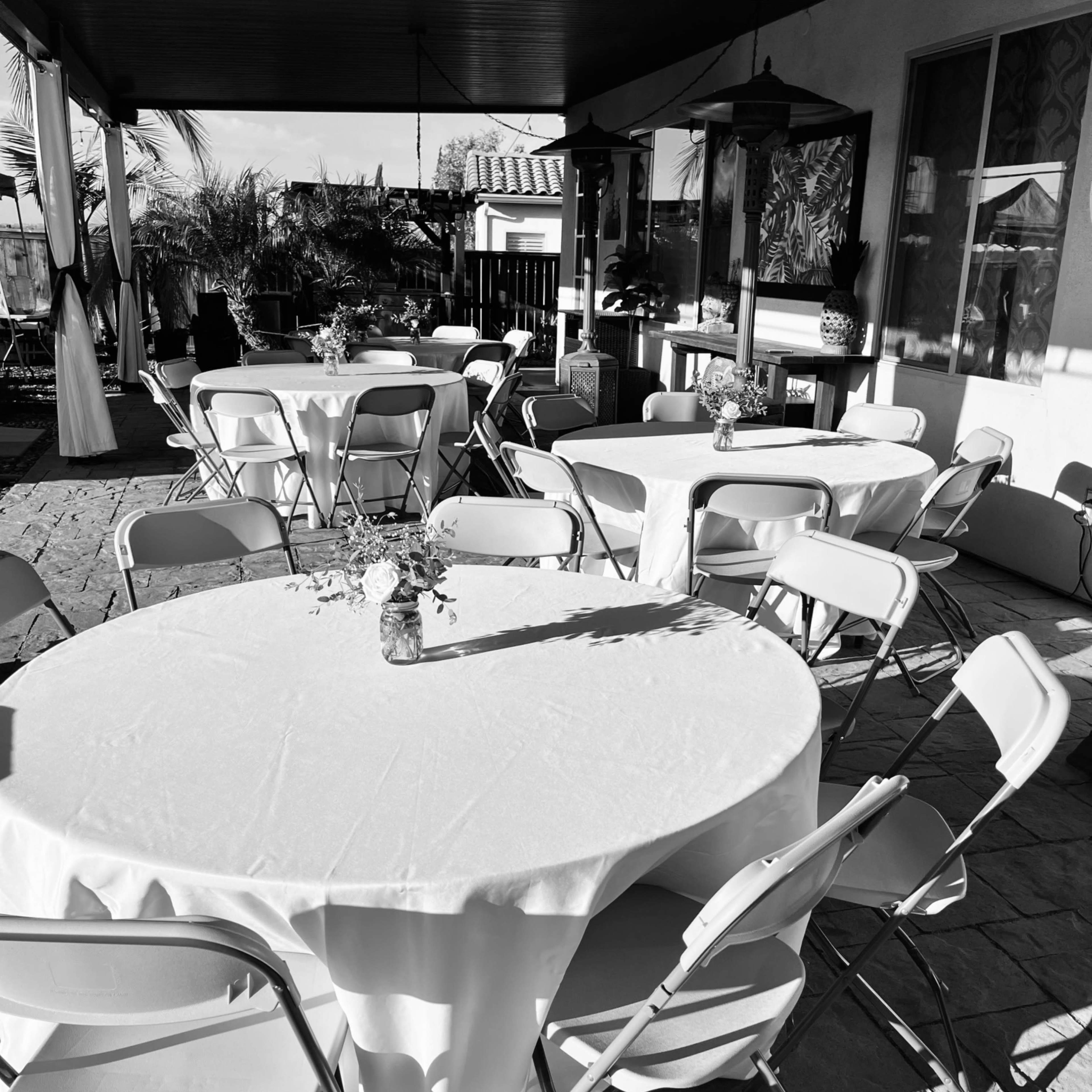 Several round tables set with white tablecloths and chairs arranged on a patio area.