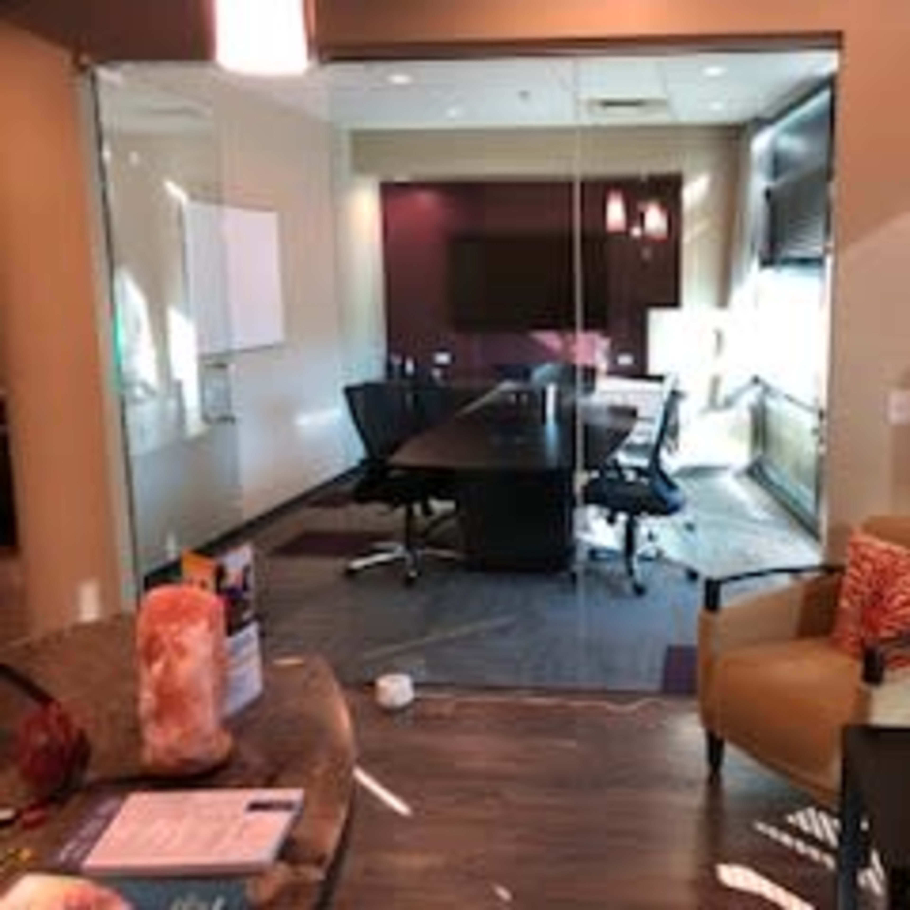 A modern conference room with a large table, black chairs, and a wall-mounted screen, featuring a partially glass wall and warm lighting.