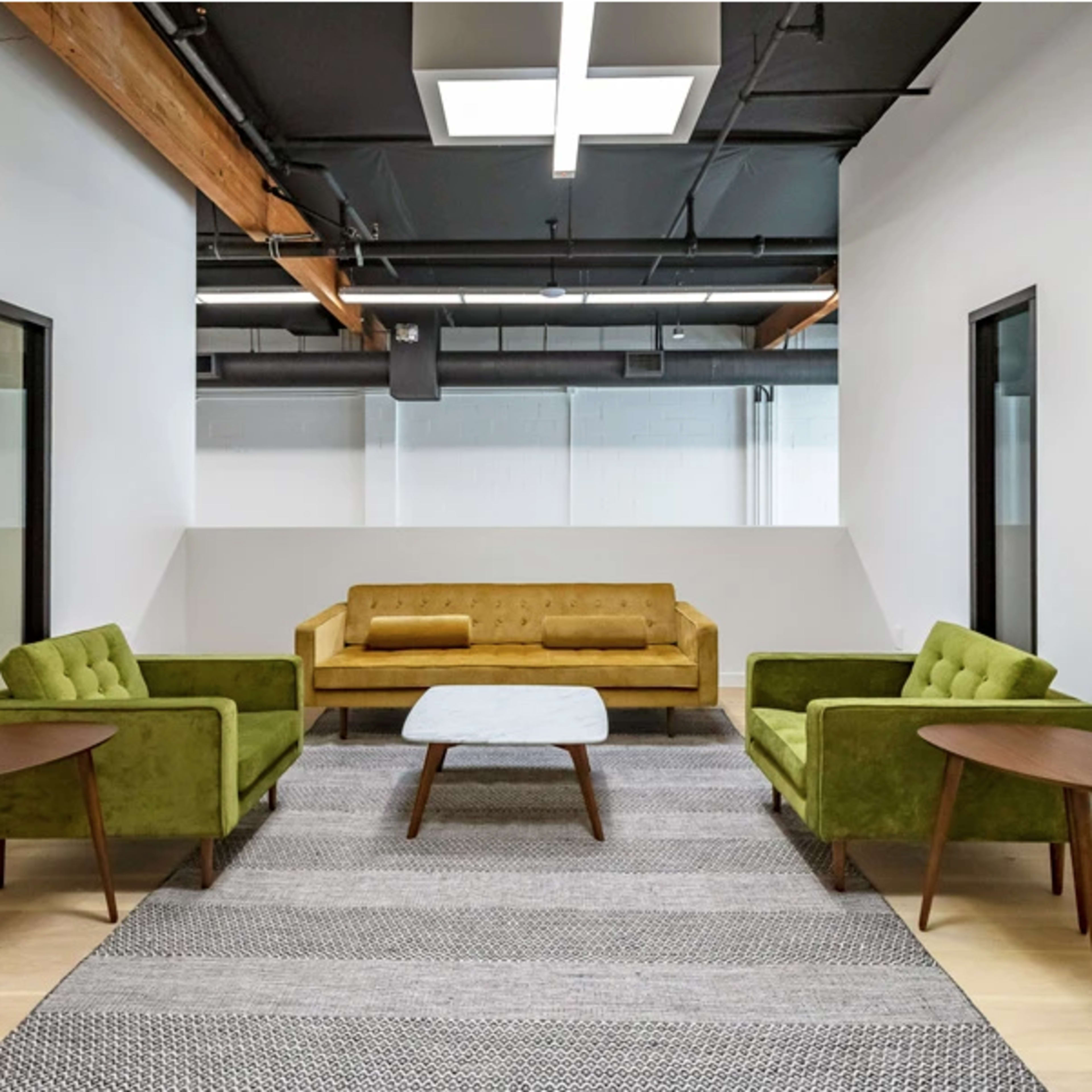 A modern, minimalistic lounge area featuring a yellow sofa, two green armchairs, a white coffee table, and a patterned rug on light wooden flooring.
