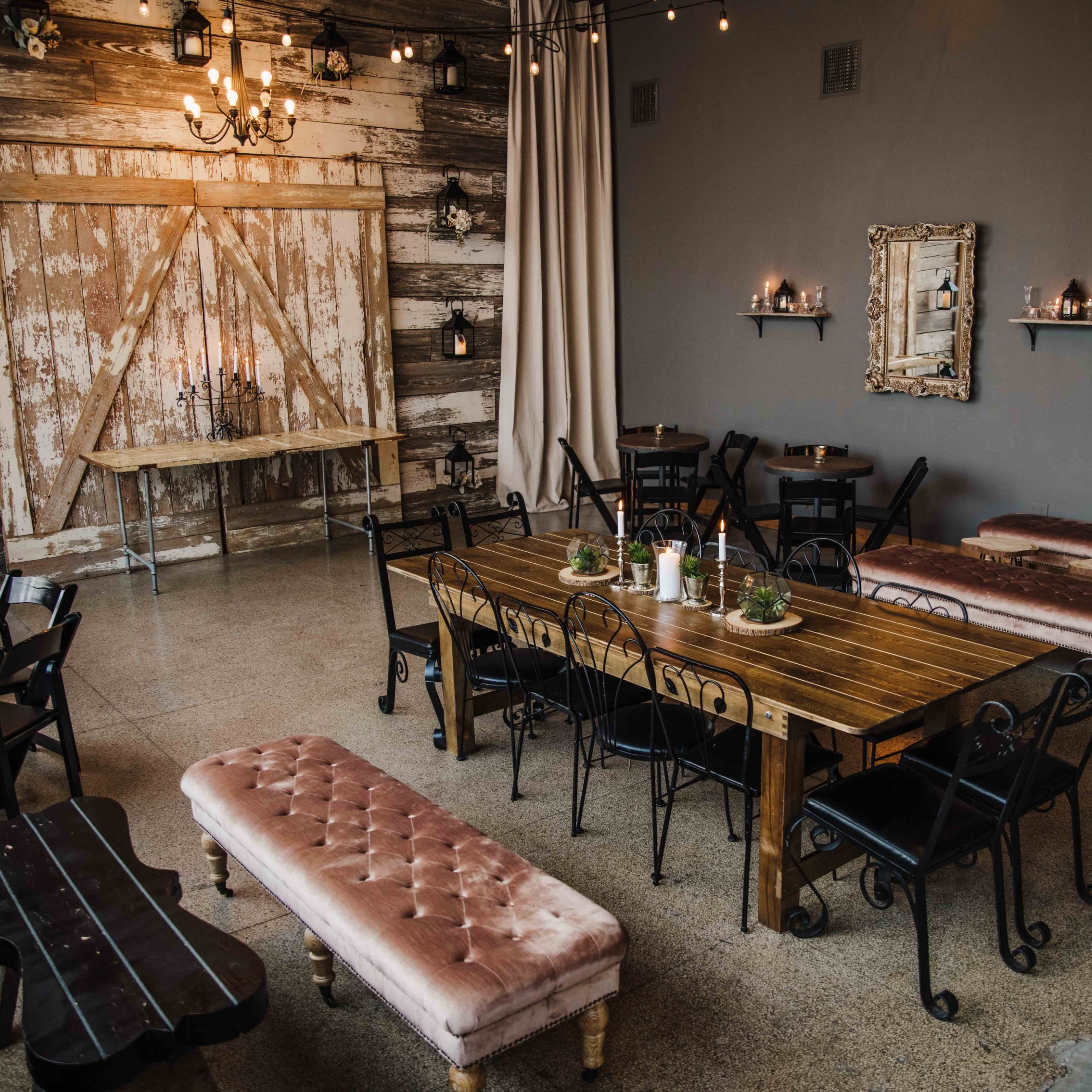 A rustic dining area with a large wooden table, several smaller tables, and benches, all arranged beneath warm lighting and decorative wall features.