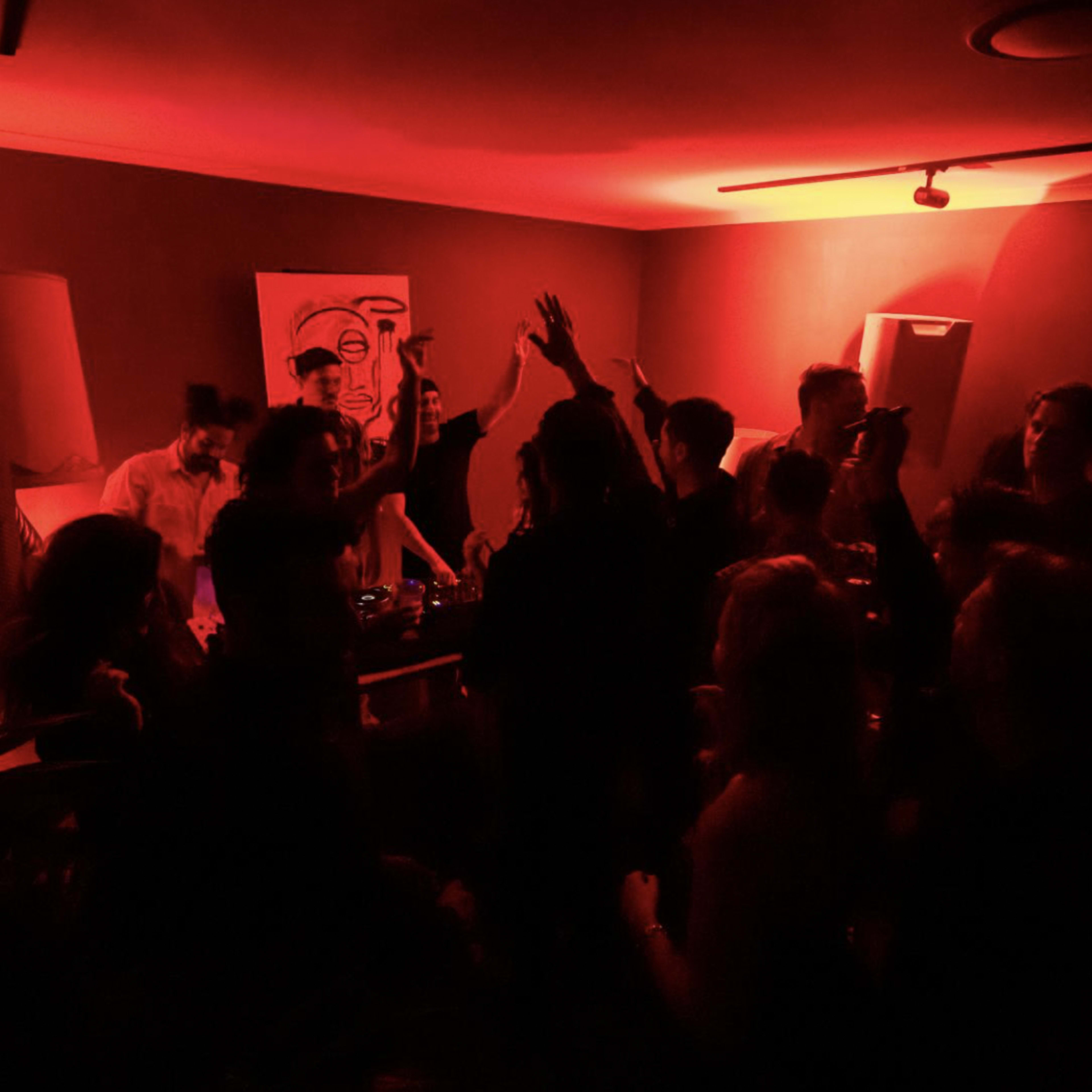 A group of people dance and enjoy music in a dimly lit room with red lighting and large speakers.