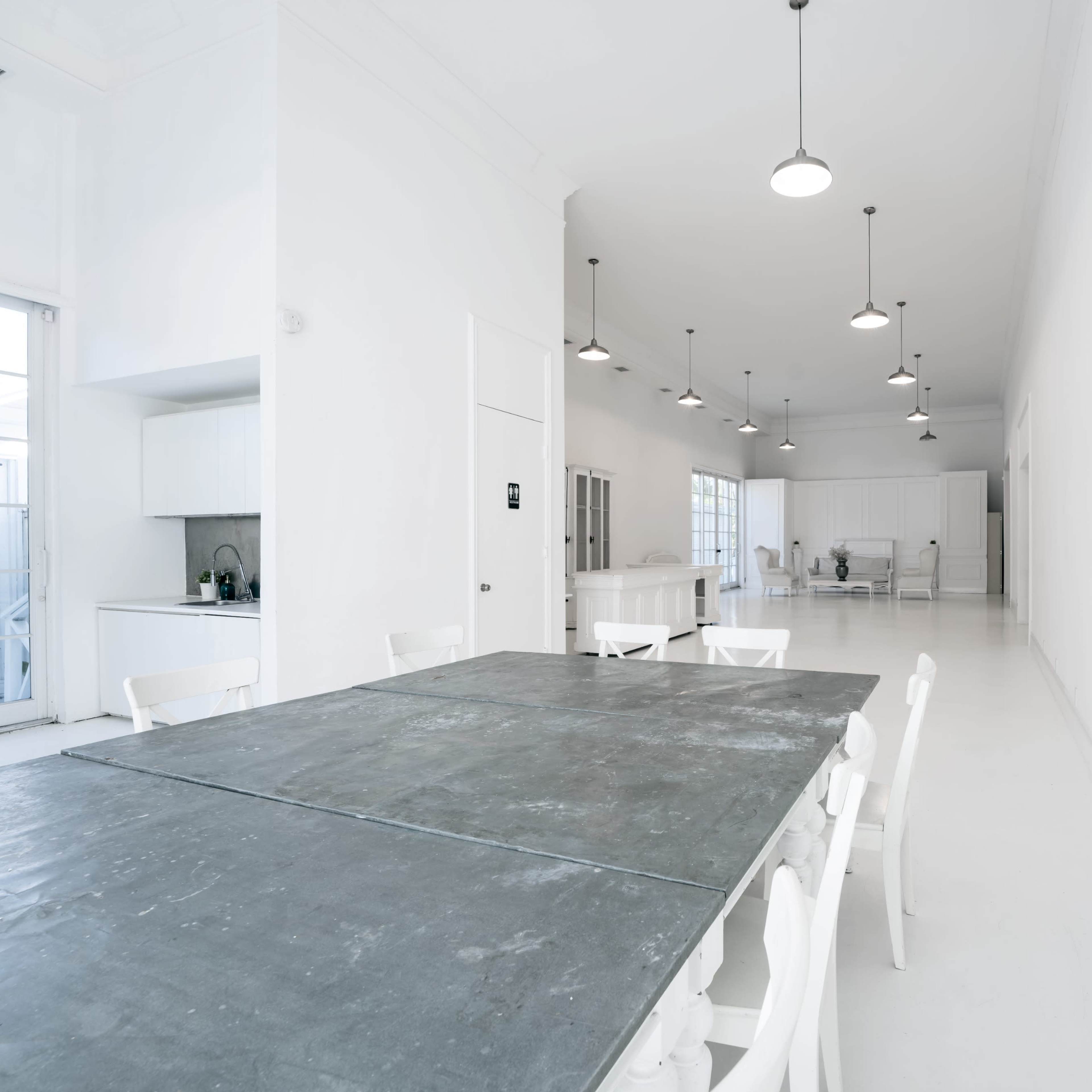 A spacious, brightly lit room with white walls and a long, gray table surrounded by white chairs.