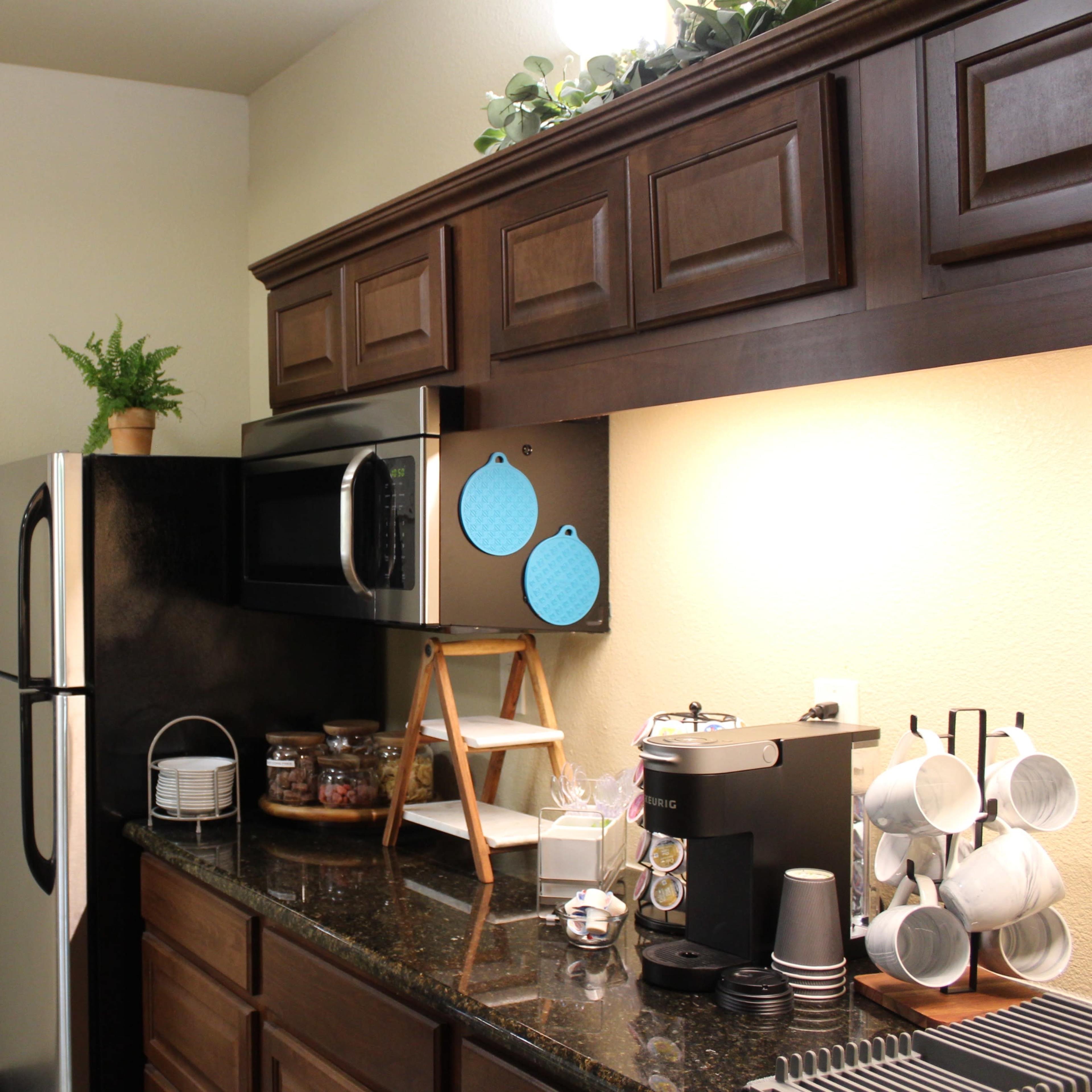 The kitchen features dark wooden cabinets, a stainless steel refrigerator, a microwave, and a countertop with a coffee maker and various kitchenware.