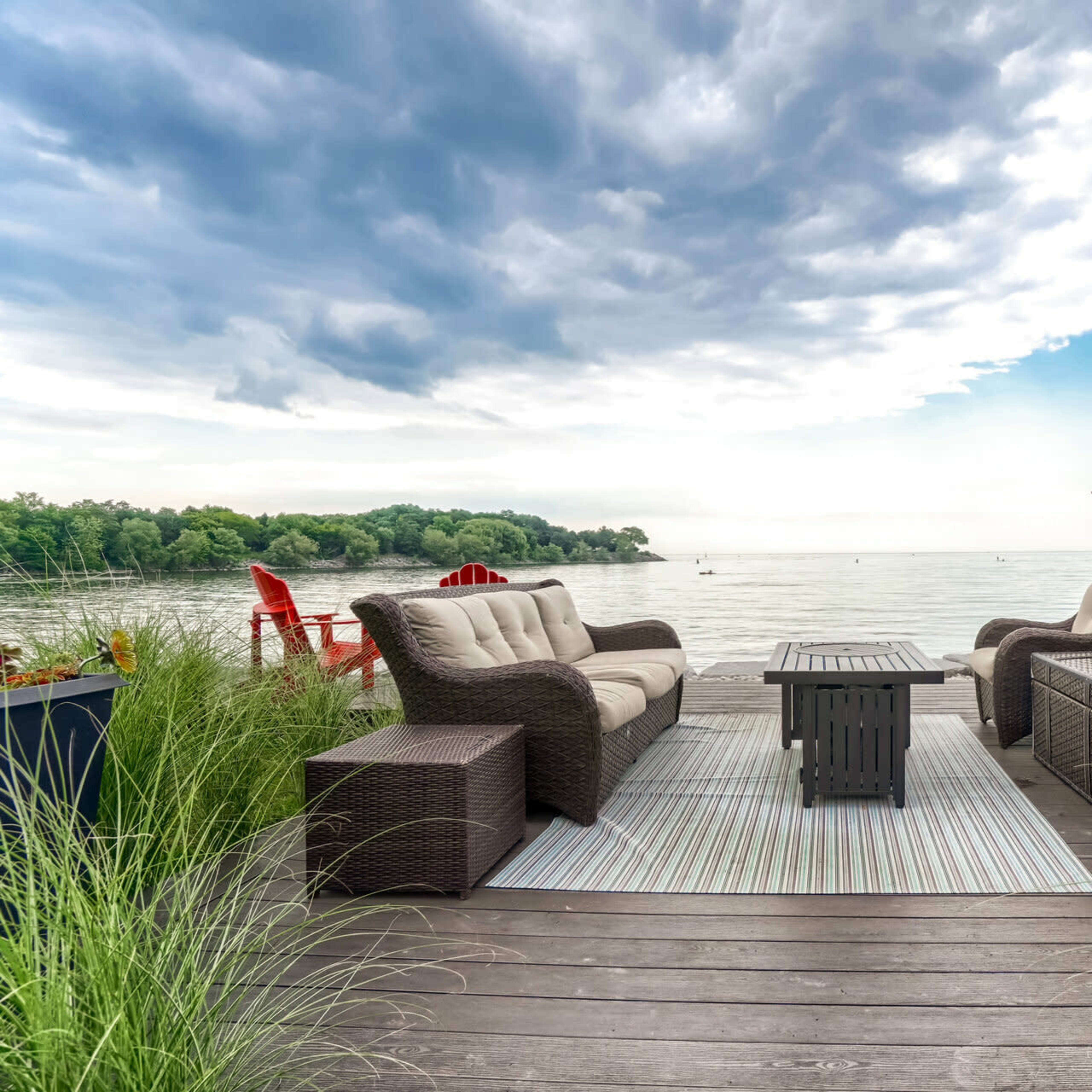 A seating area with two sofas and a coffee table overlooks a calm lake with trees in the background.