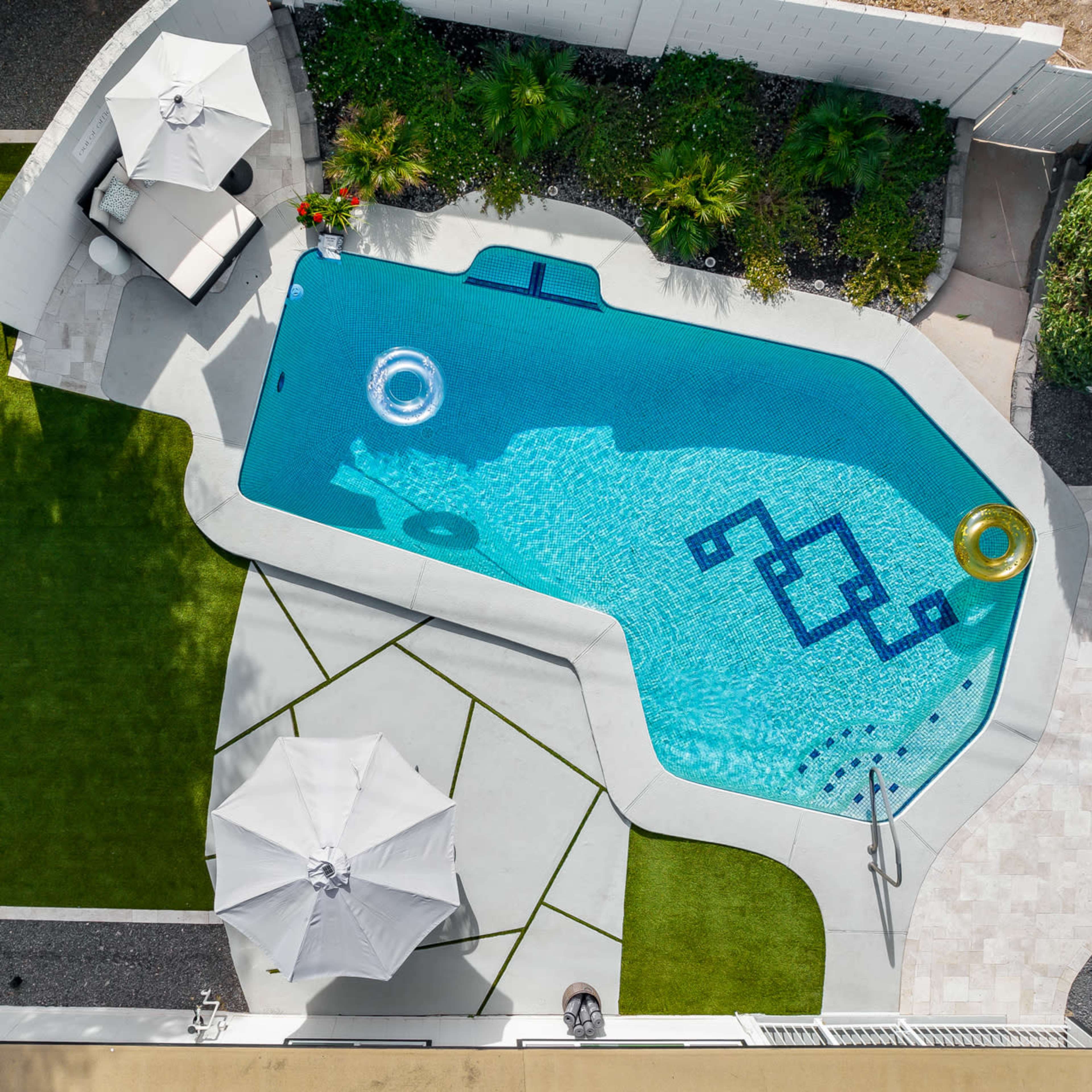 An aerial view of a landscaped backyard featuring a swimming pool, lounge chairs, and various plants.