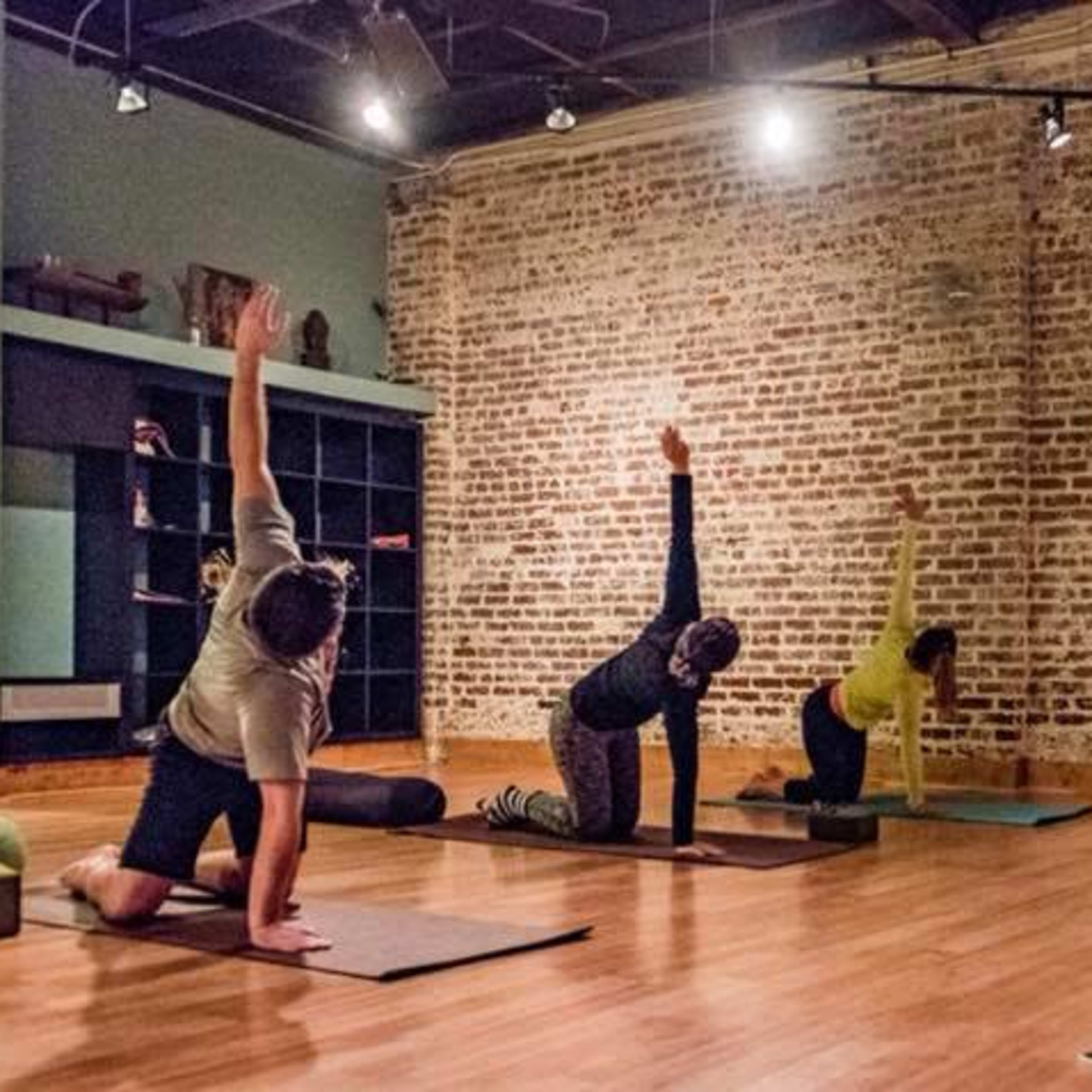 A group of six people is practicing yoga on mats in a studio with exposed brick walls.