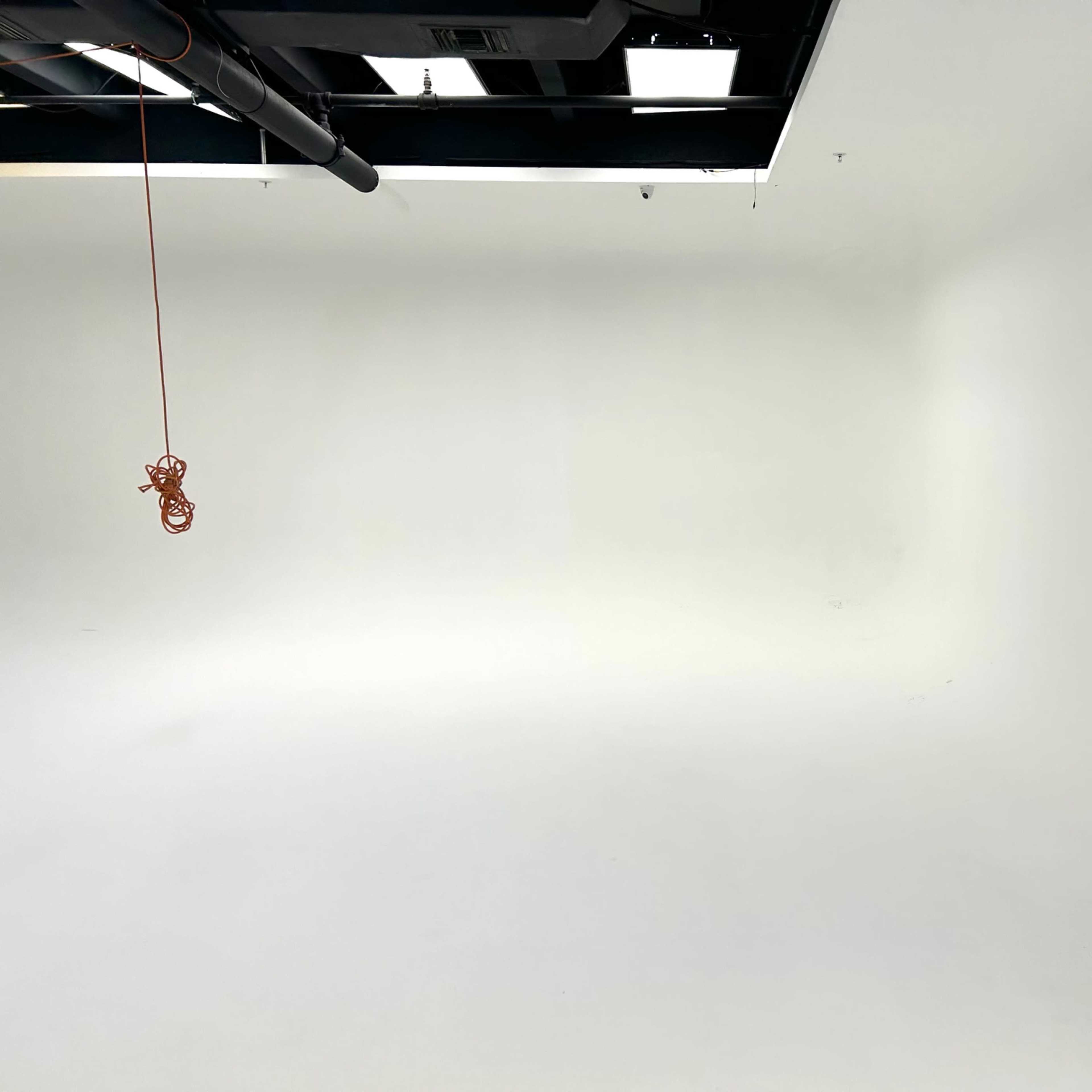 An empty studio space with a white backdrop and a hanging cable.