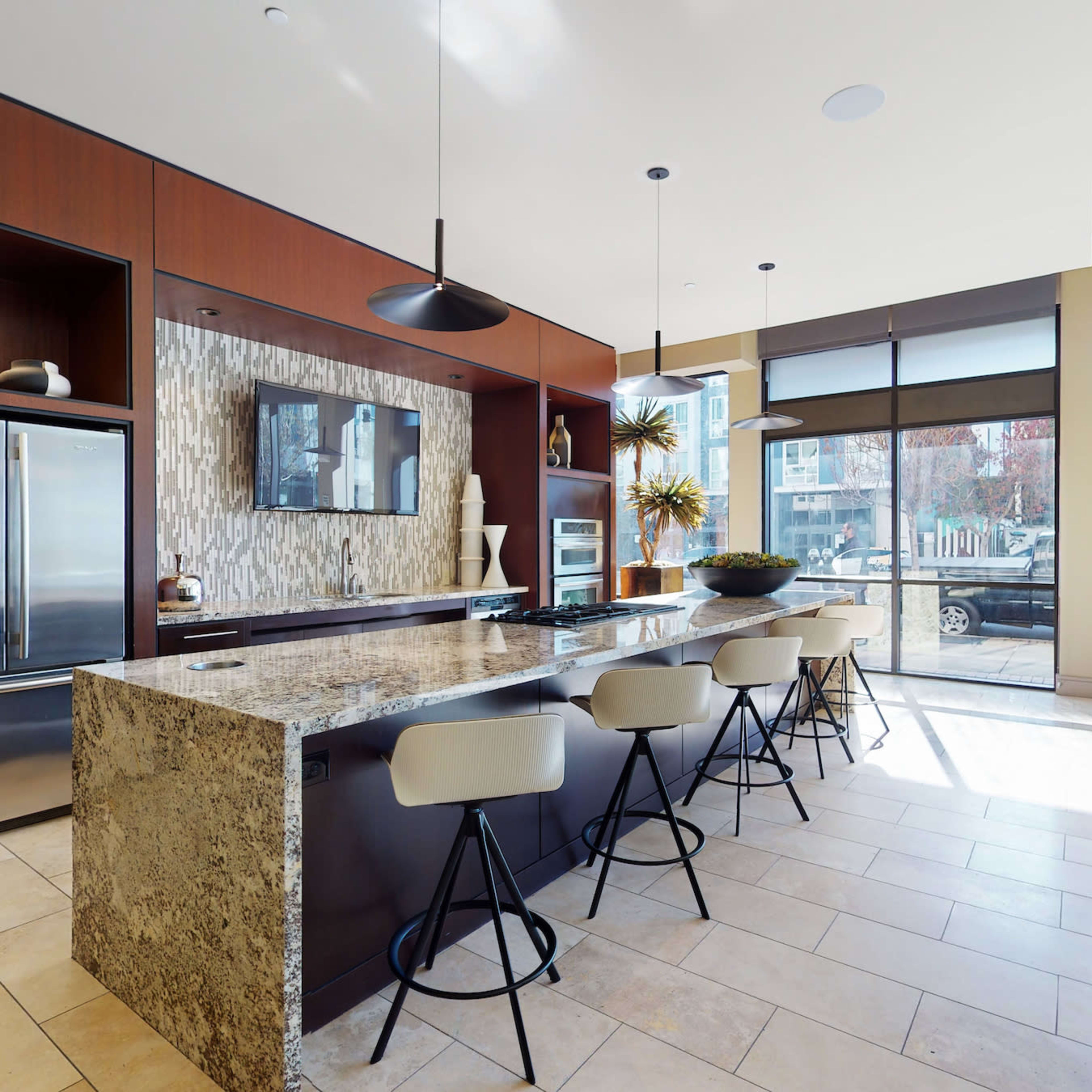 A modern kitchen with a large stone island, bar stools, stainless steel appliances, and windows that let in natural light.