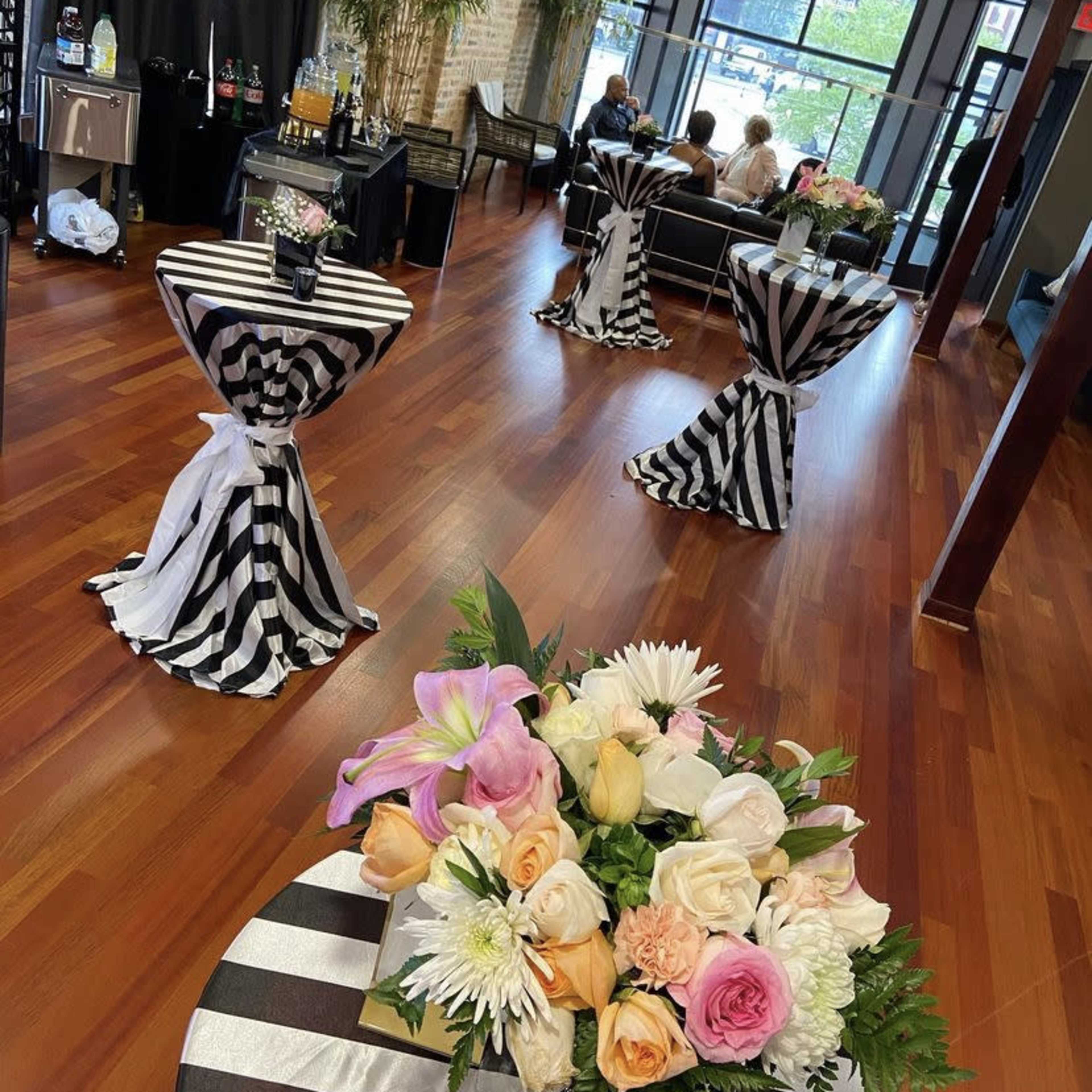 A reception area with black and white striped tables adorned with floral arrangements, set against a backdrop of wooden flooring and modern furnishings.