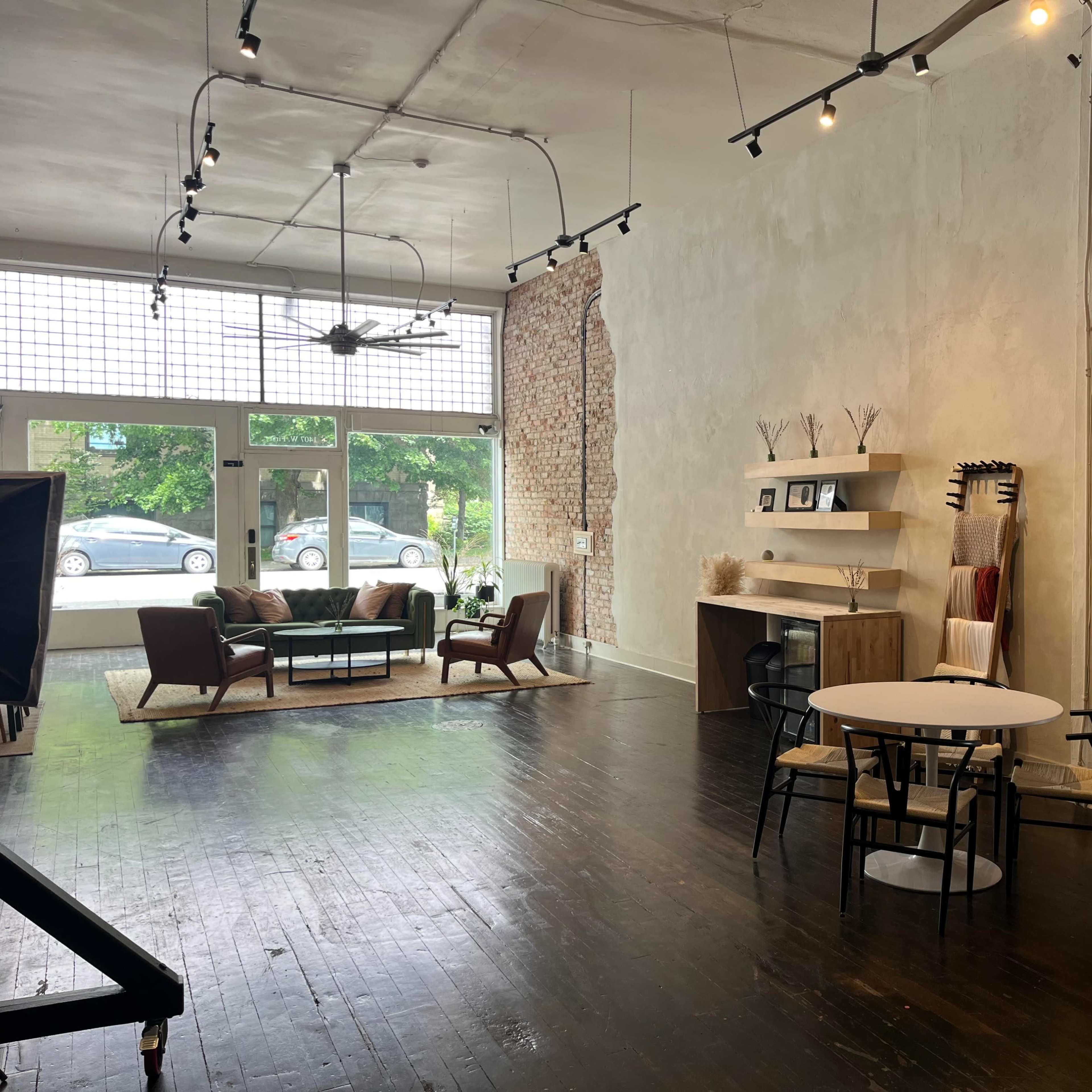 A spacious, modern interior with a seating area, a dining table, and shelves against textured walls, illuminated by overhead lights.
