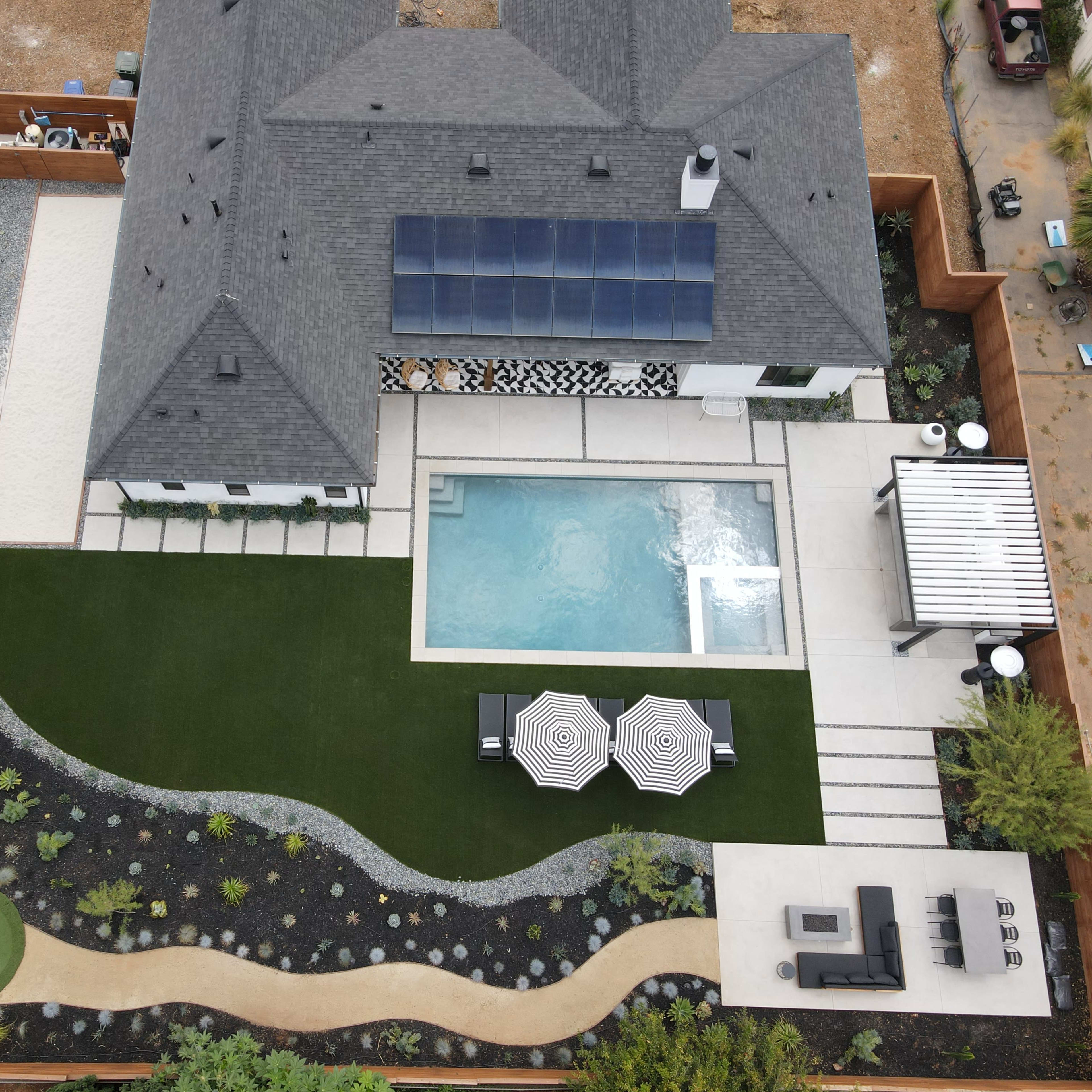 An aerial view of a residential backyard featuring a swimming pool, a landscaped garden with a putting green, and multiple seating areas.