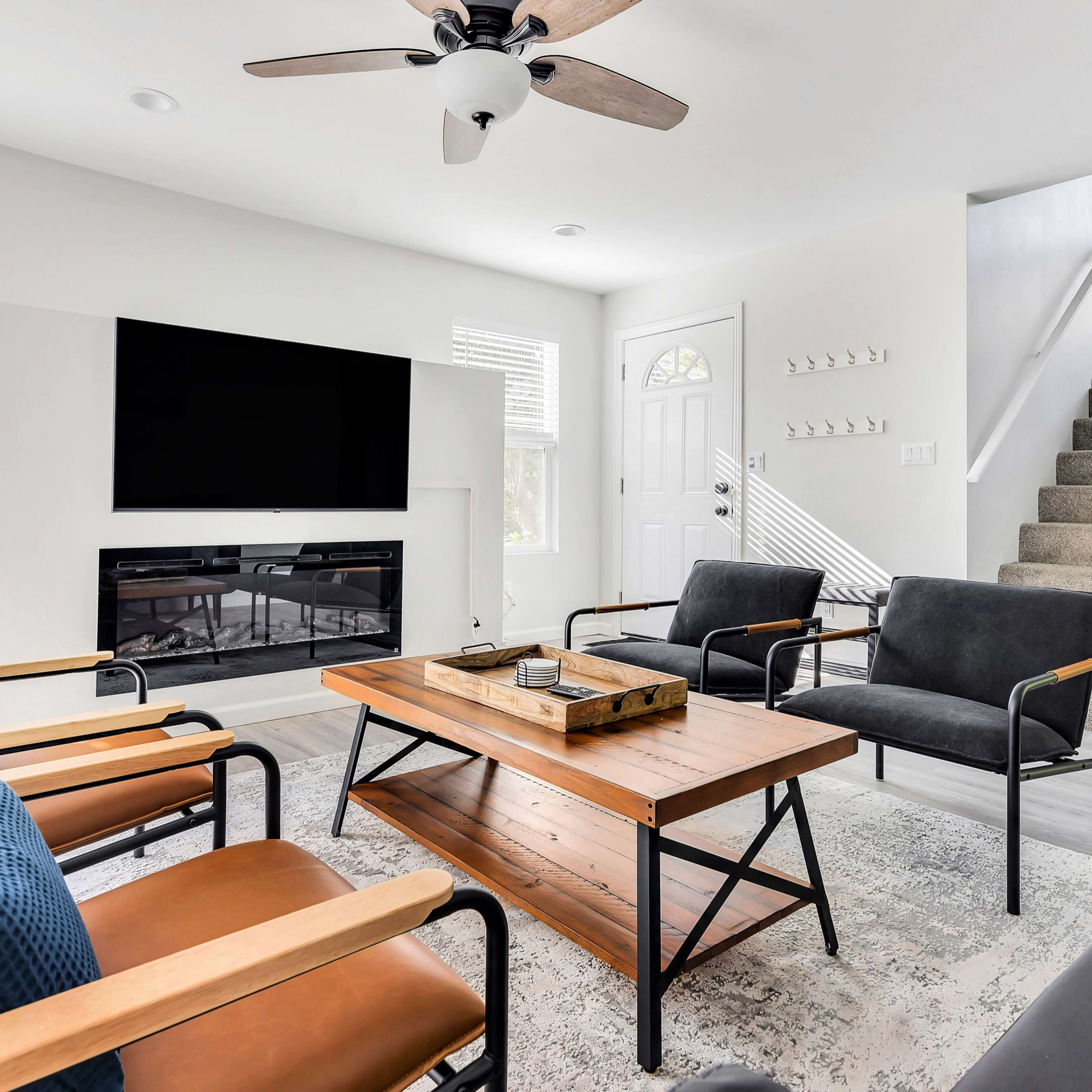The living room features a modern design with a television mounted on the wall, a wooden coffee table, and seating arranged around it, along with stairs leading to a second level.