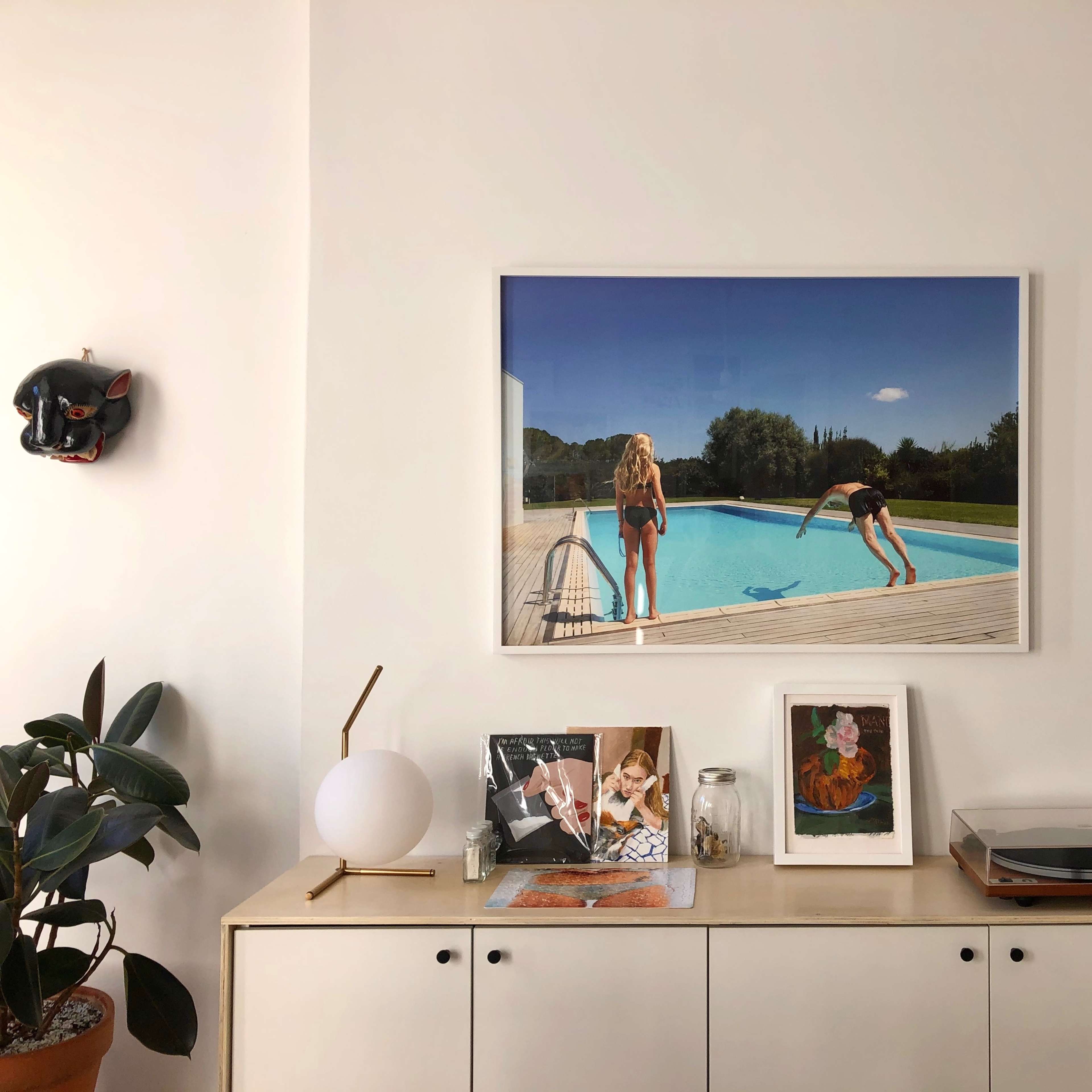 A framed photograph of two women near a swimming pool, displayed on a wooden sideboard alongside various decorative items and a plant.