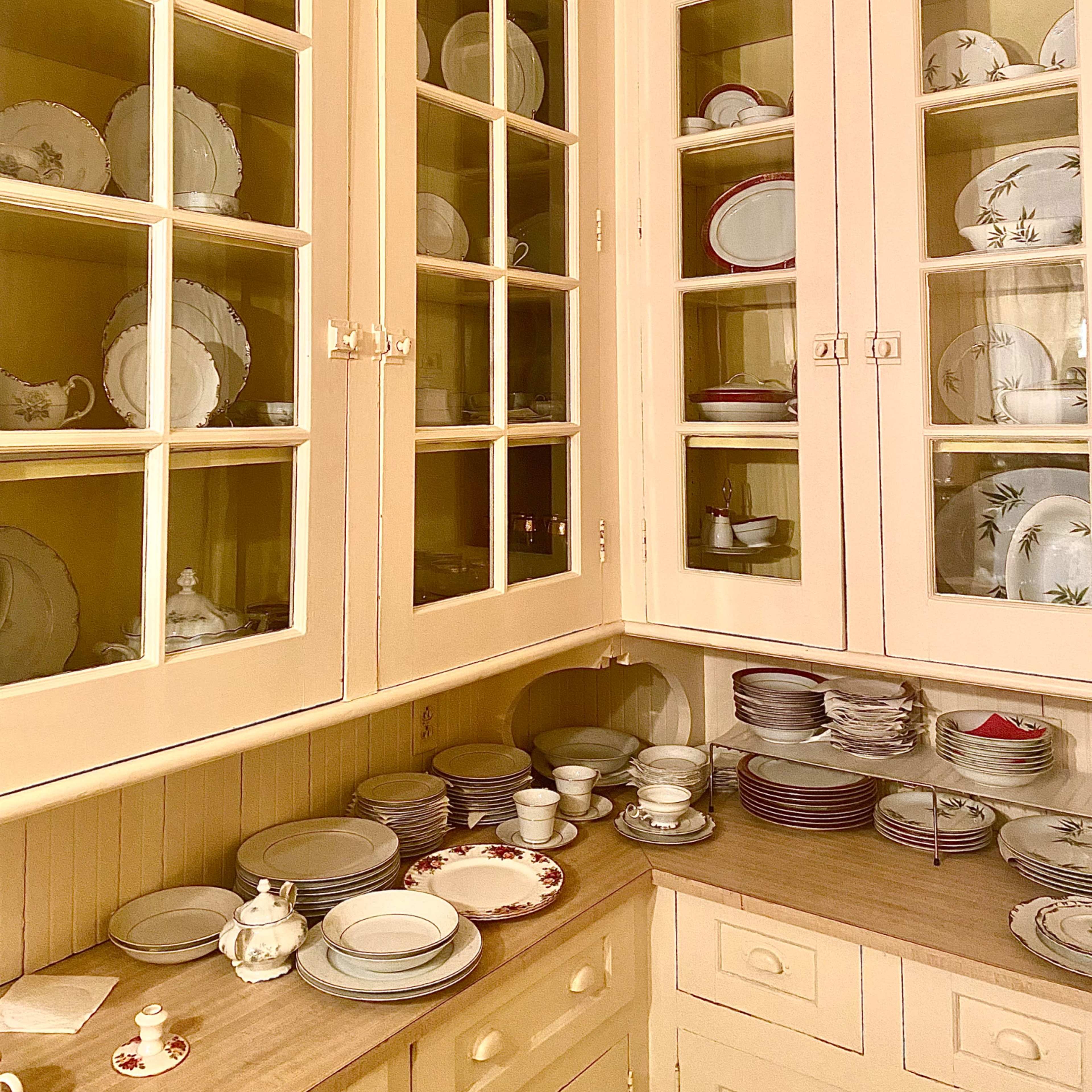 A wooden cabinet is filled with neatly arranged plates and dishes, while additional tableware is placed on the counter below.