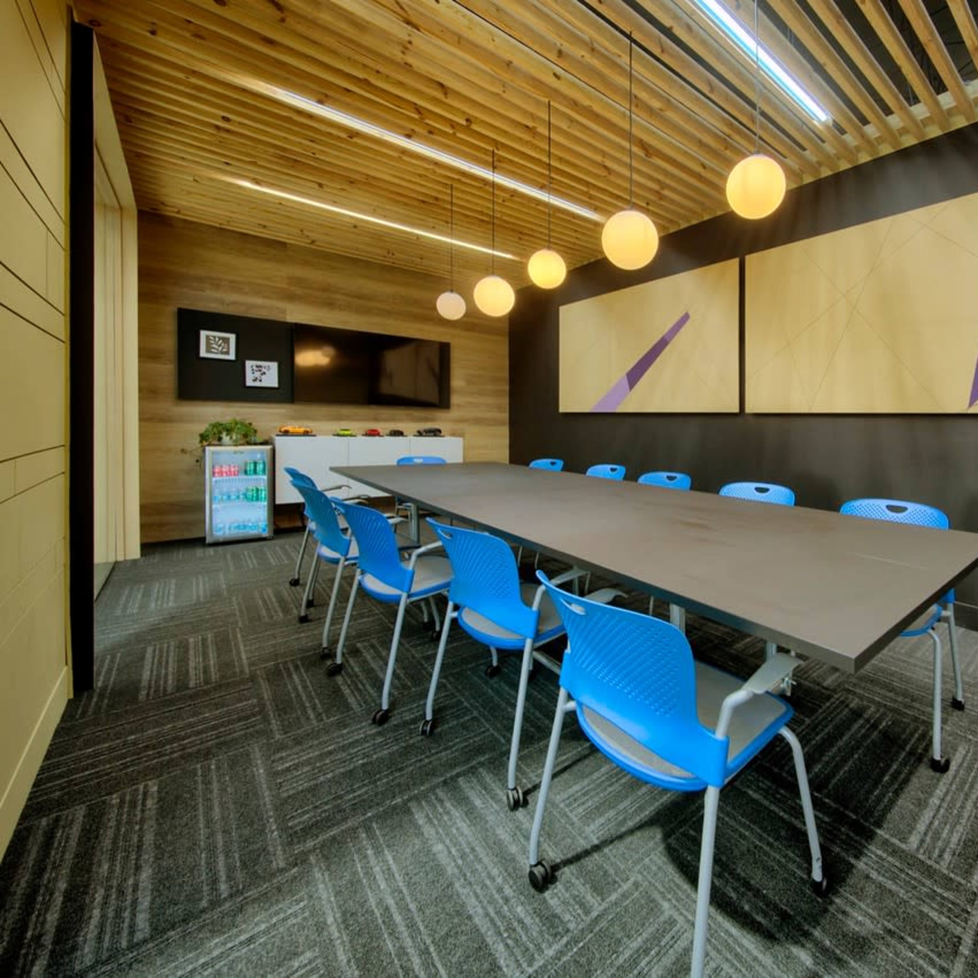 A modern conference room featuring a long table surrounded by blue chairs, with decorative wall panels and pendant lights overhead.