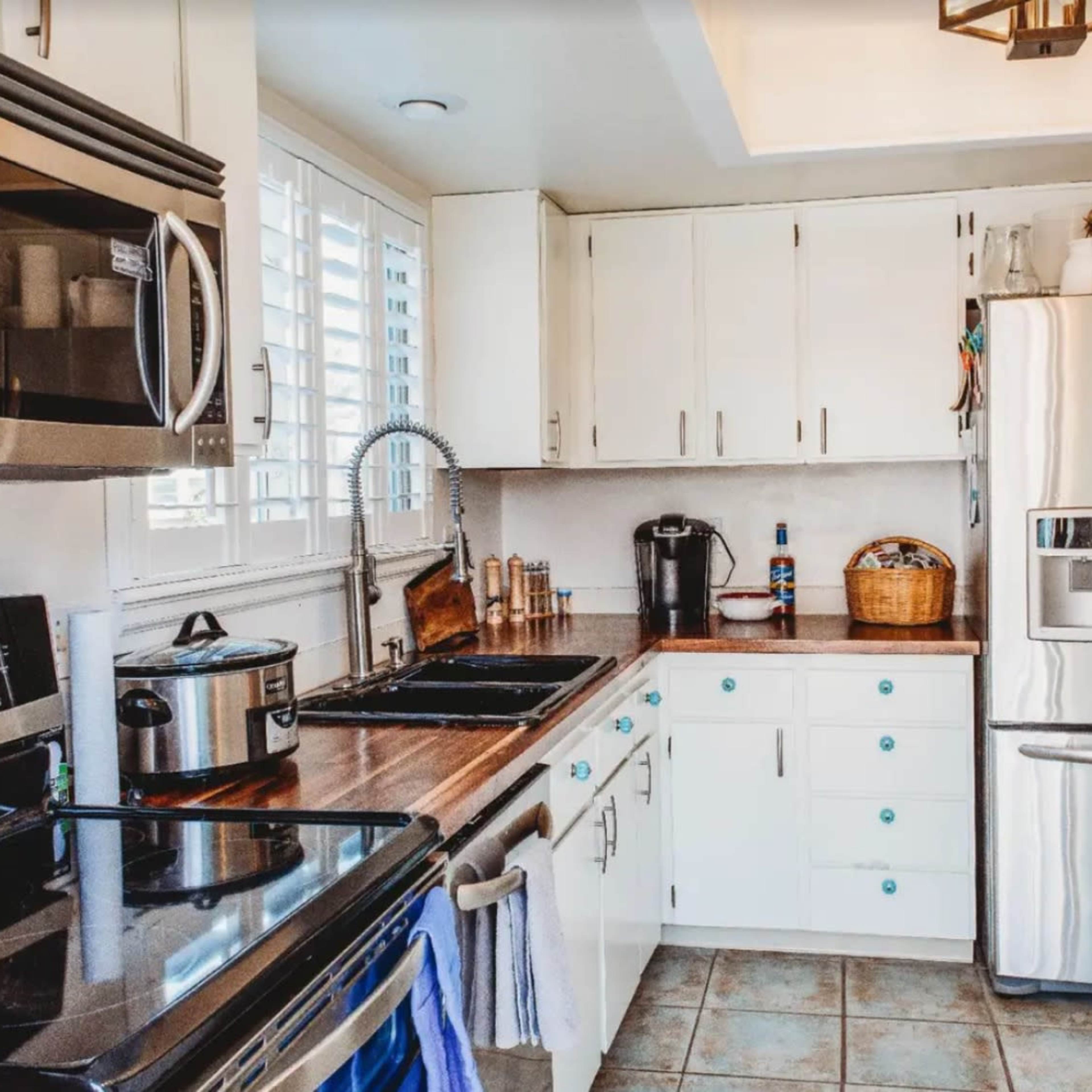 A modern kitchen features stainless steel appliances, white cabinetry with teal knobs, and a wooden countertop.