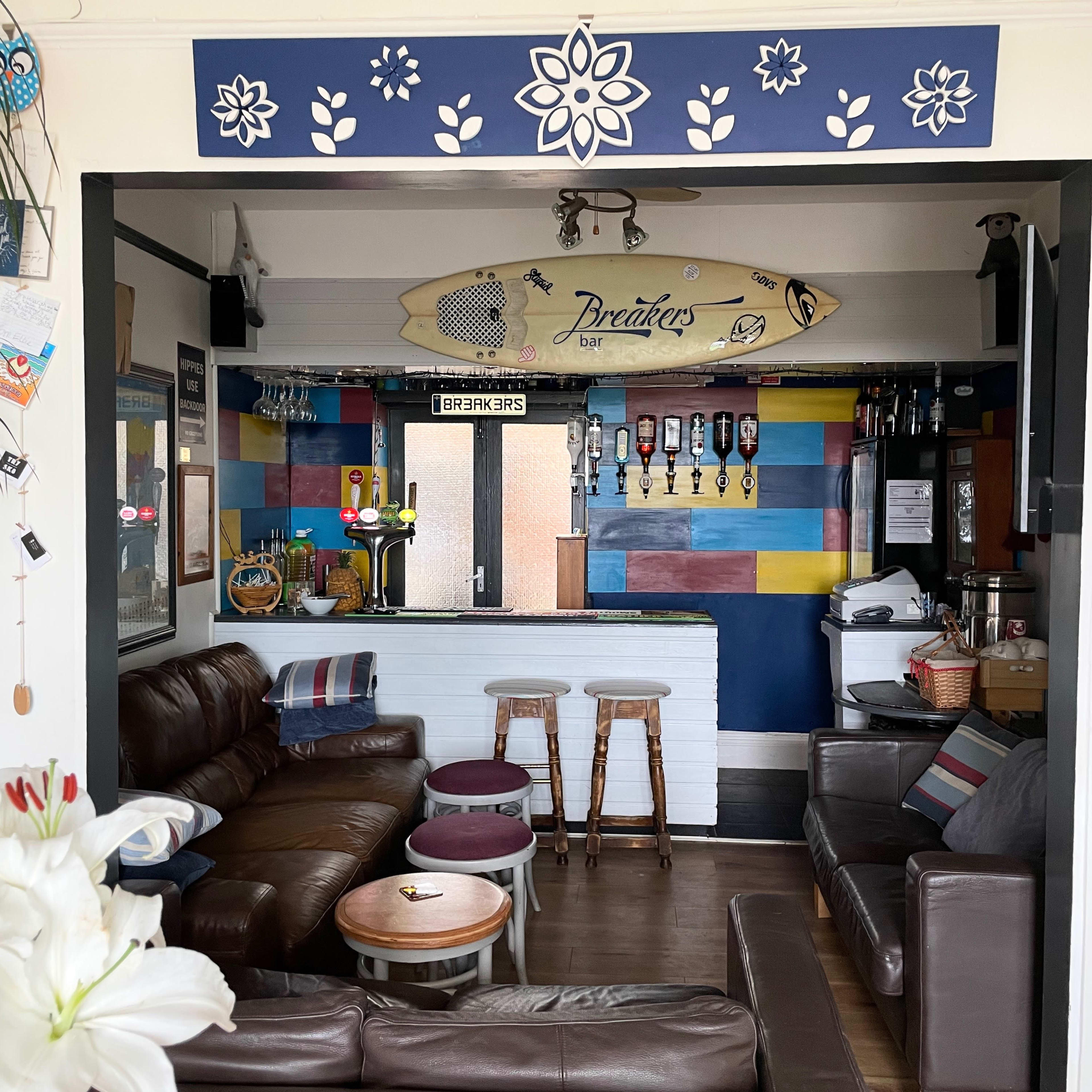 A cozy bar area featuring a surfboard, colorful wall decor, and comfortable seating.