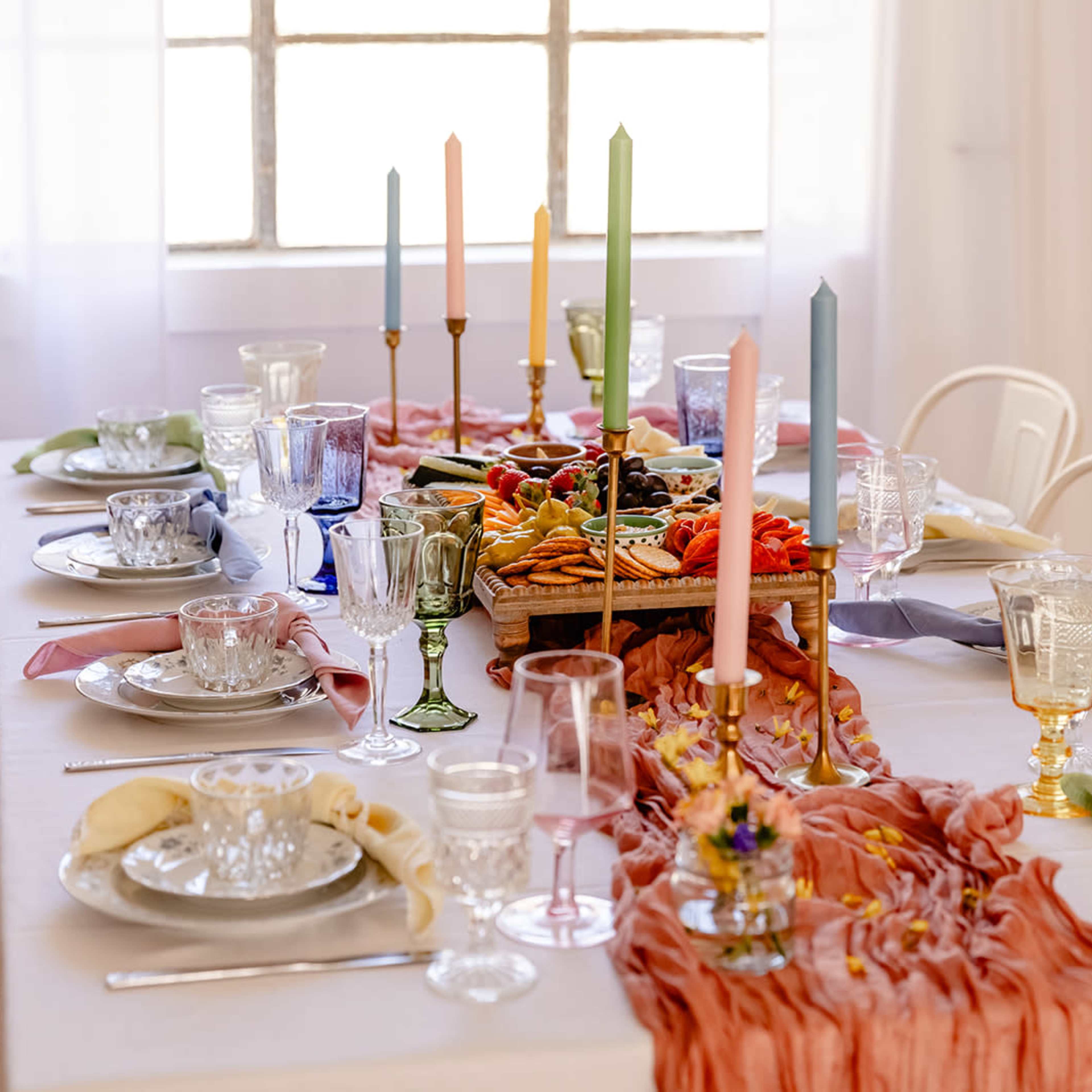 A dining table is elegantly set with various dishes, glassware, and colorful taper candles arranged in the center.
