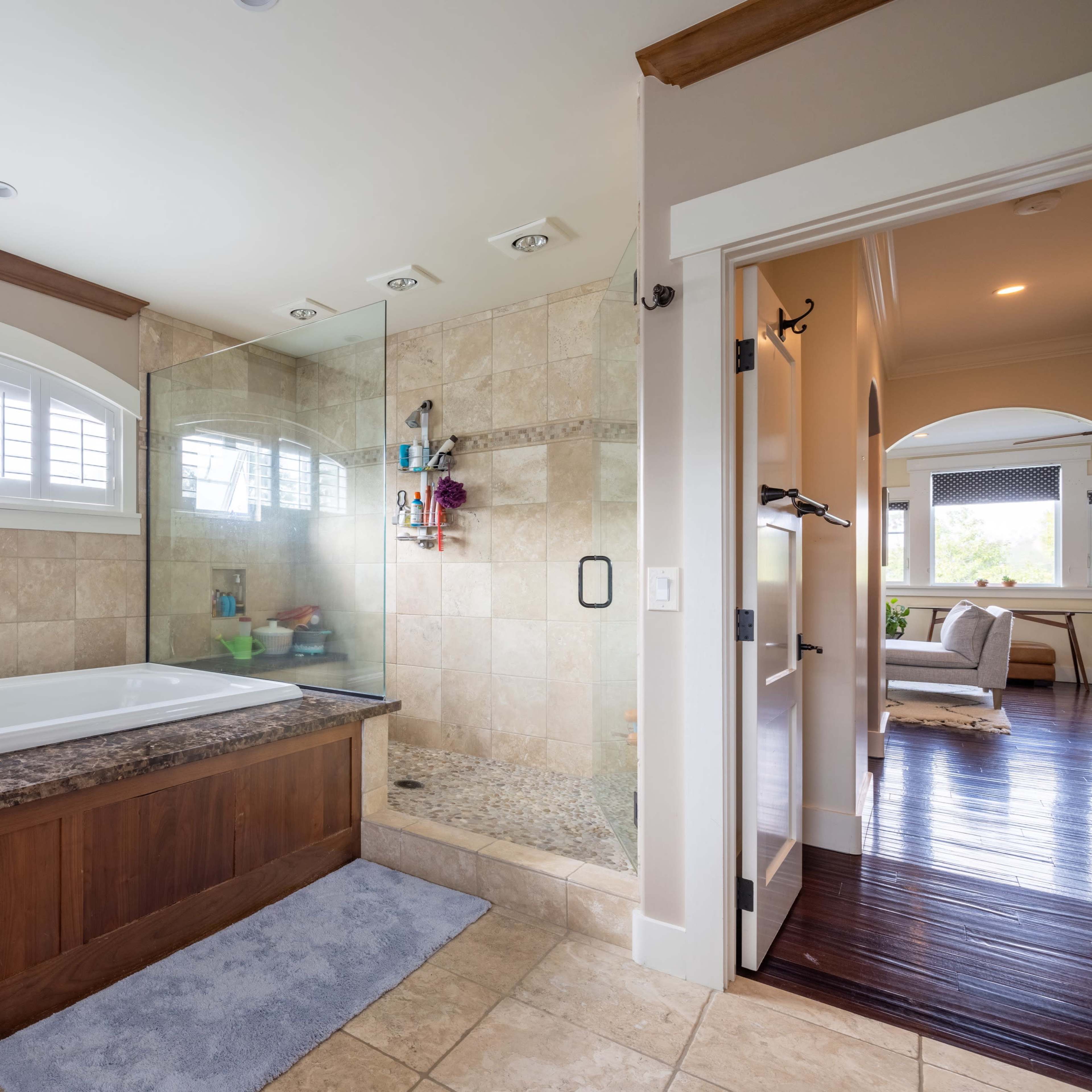 A spacious bathroom featuring a glass-enclosed shower, a large bathtub, and a window that allows natural light to enter the room.