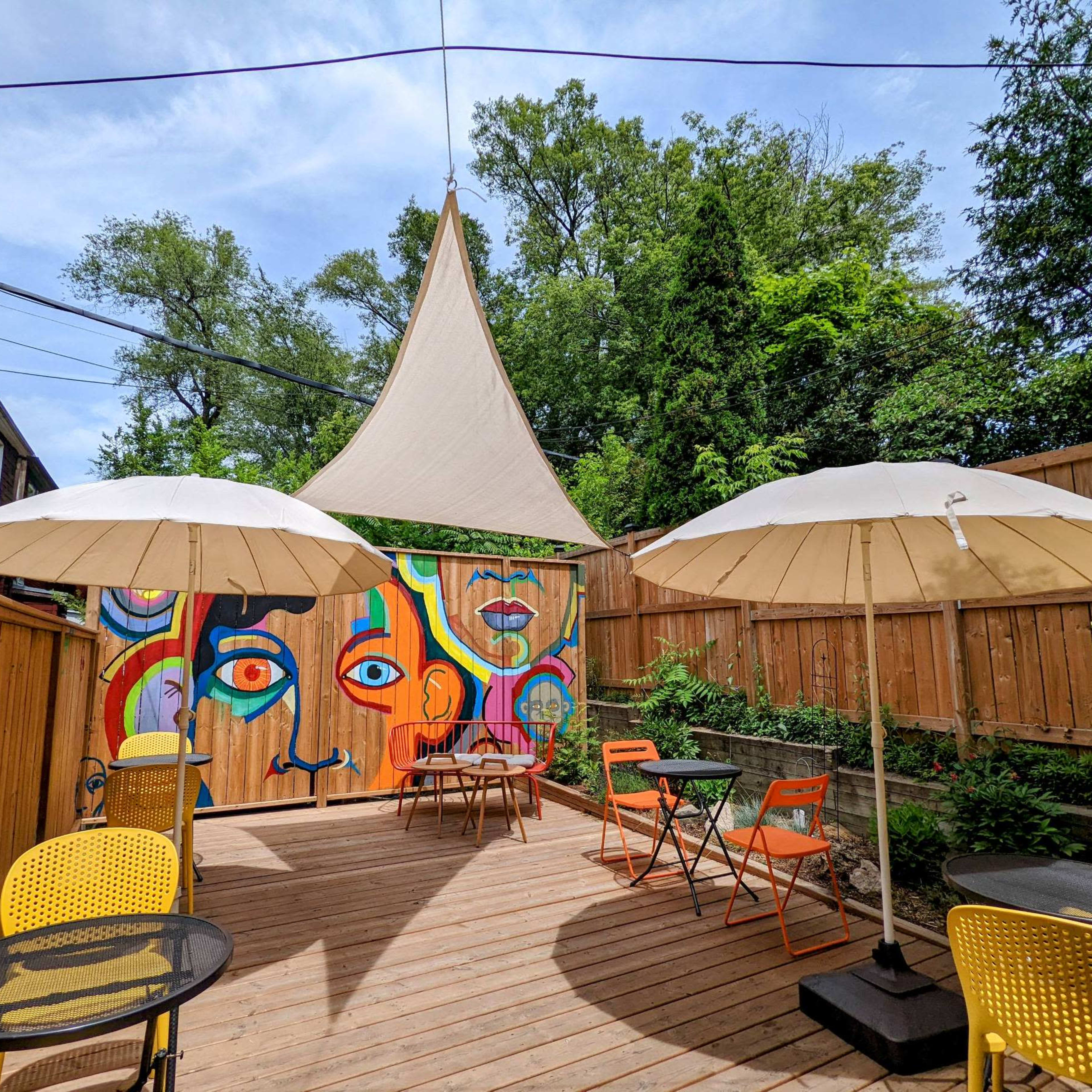 A vibrant outdoor patio features colorful murals, two large umbrellas, and a wooden deck surrounded by greenery.