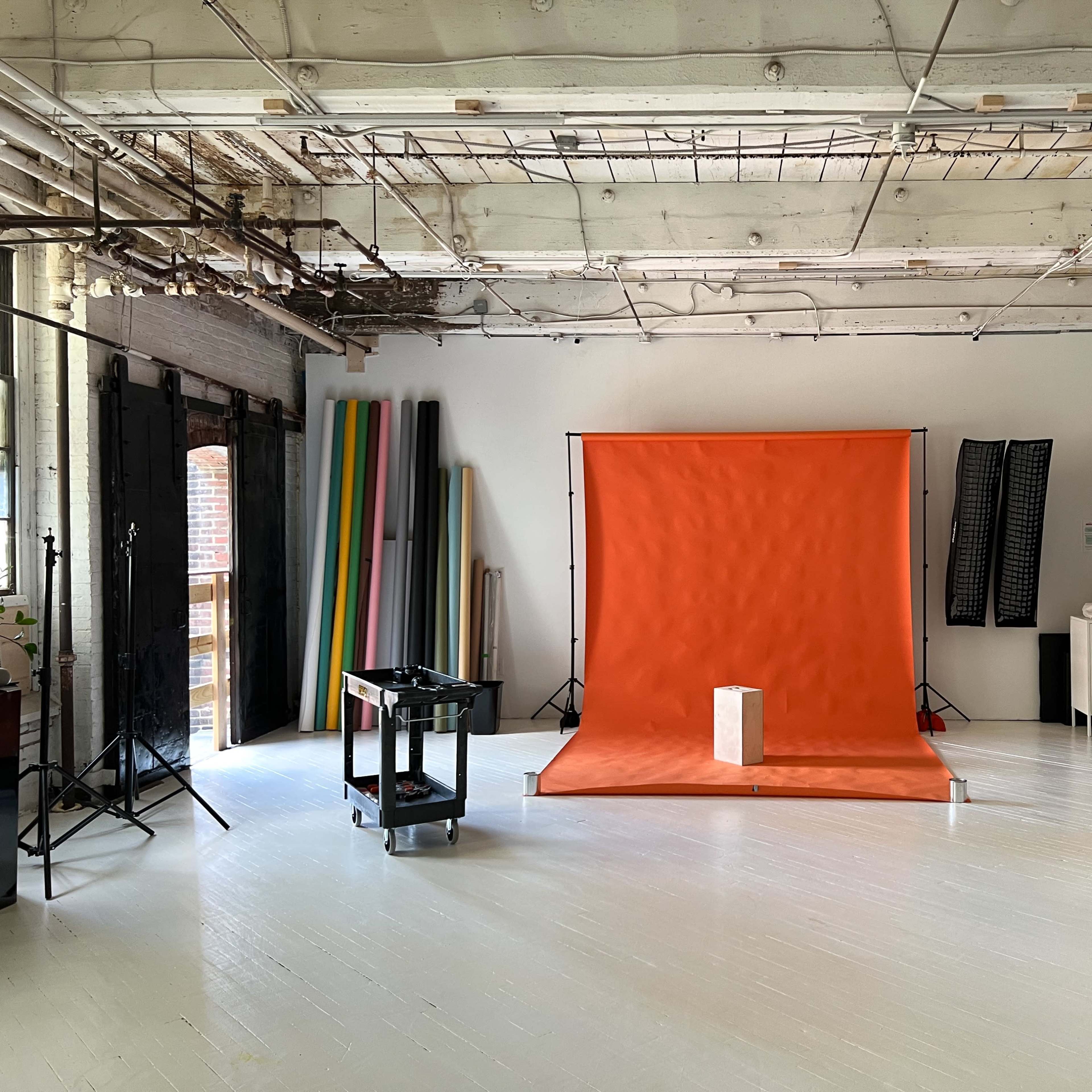 A spacious studio with an orange backdrop, various props, and equipment arranged around a bright, white floor.