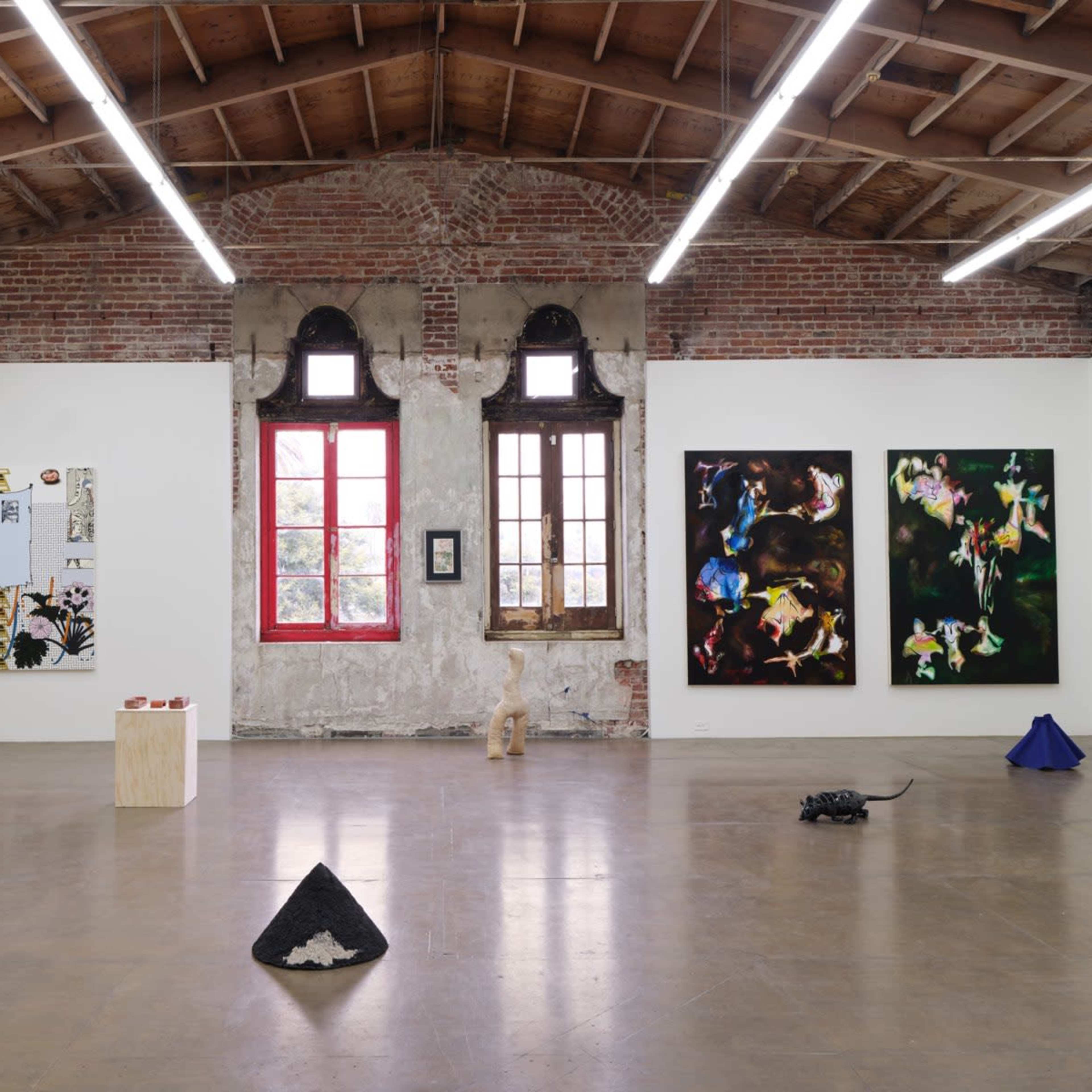 A spacious art gallery featuring various artworks, including colorful paintings on the walls and sculptural objects arranged on the floor.