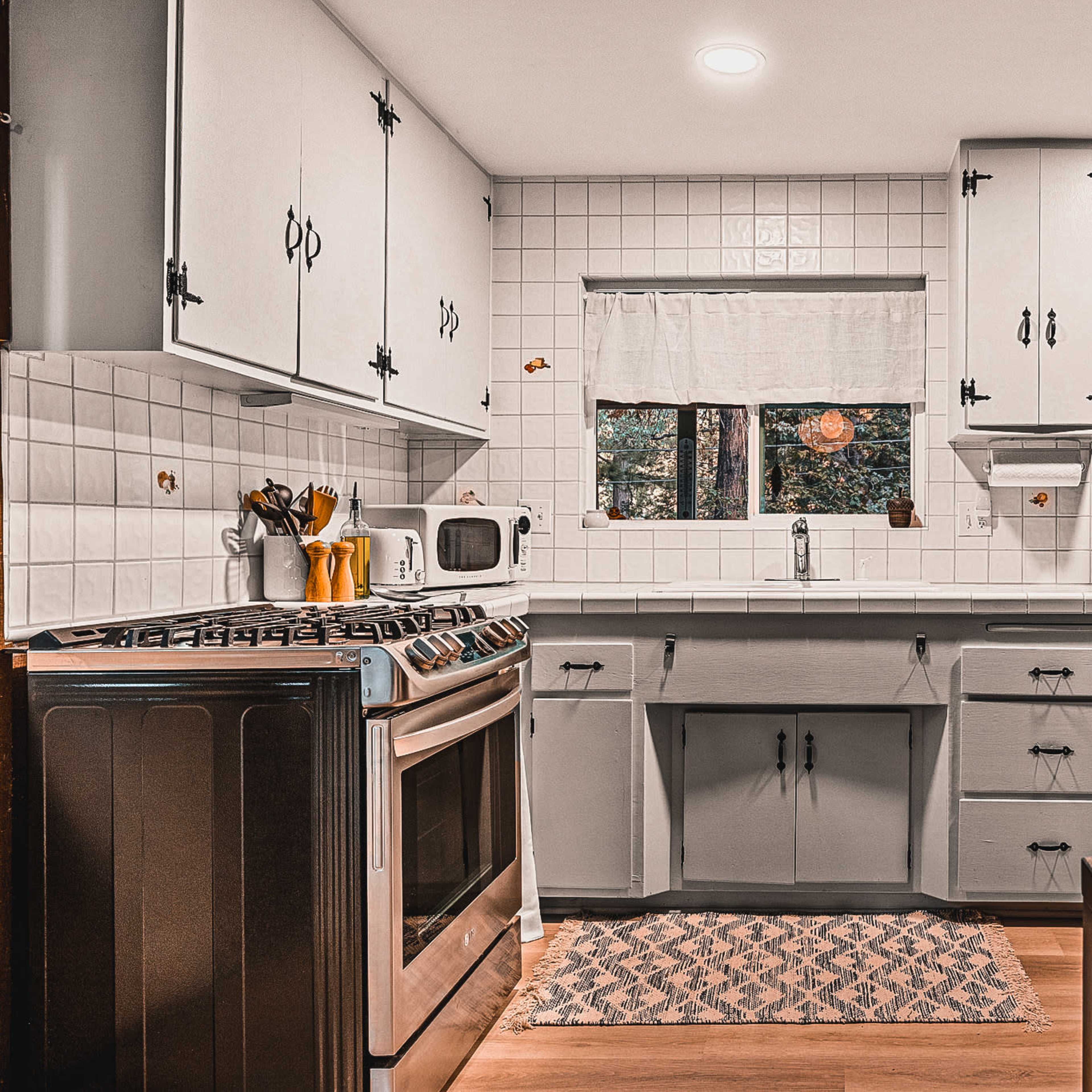A modern kitchen features stainless steel appliances, white cabinets, and a small dining area, with natural light coming through a window.
