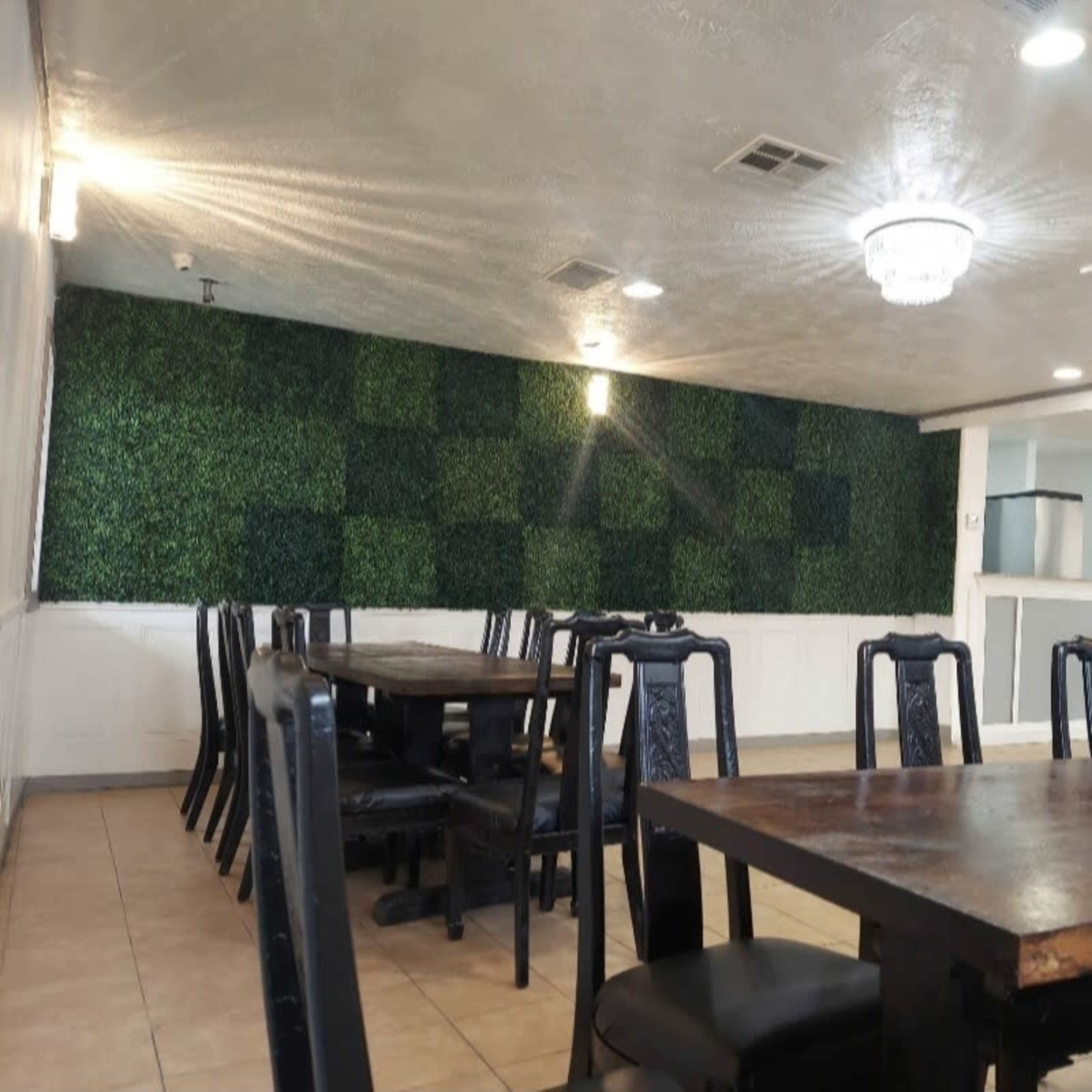 A dining area with several wooden tables and black chairs, featuring a wall covered in green foliage.
