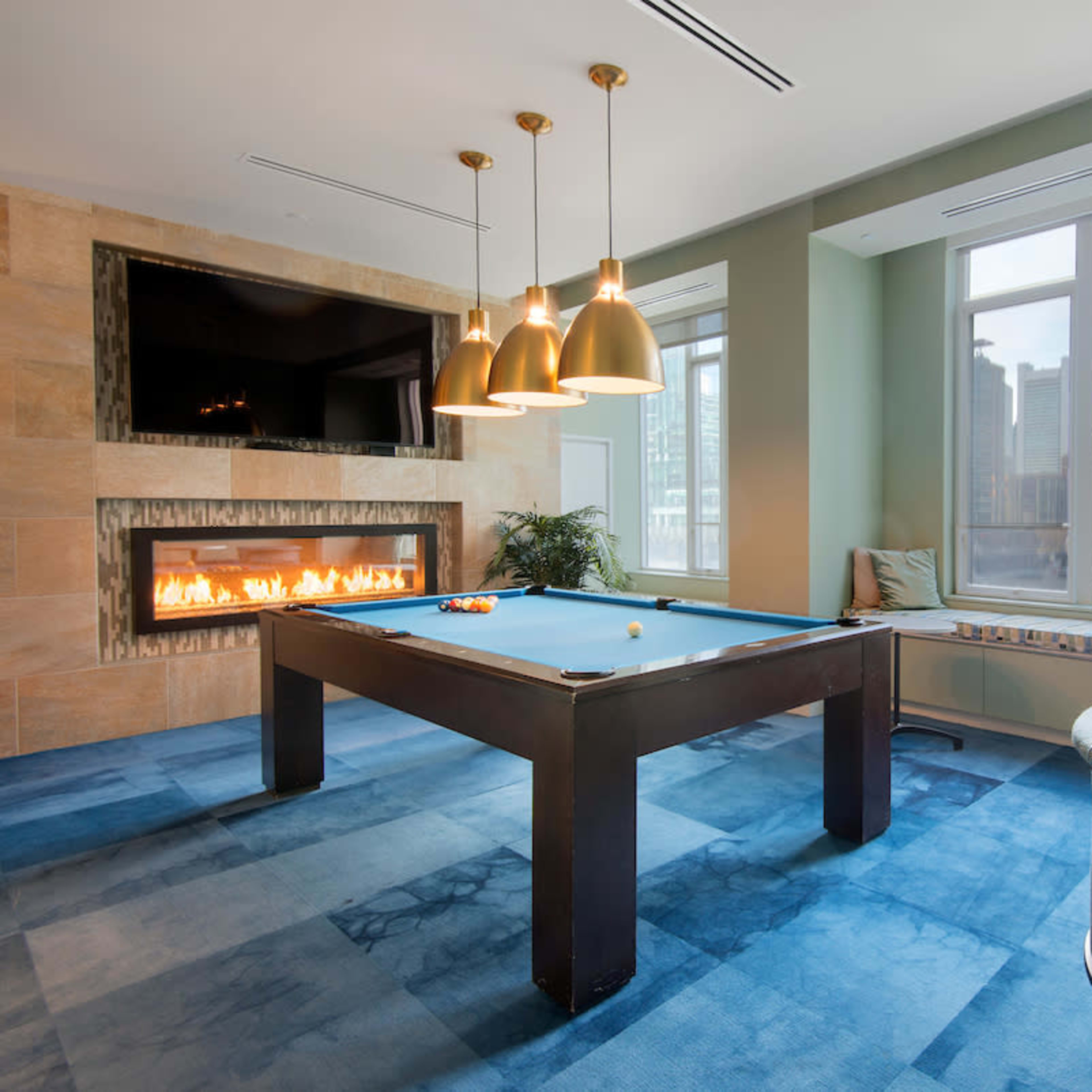 A modern game room featuring a pool table, a wall-mounted television, and large windows with a cityscape view.