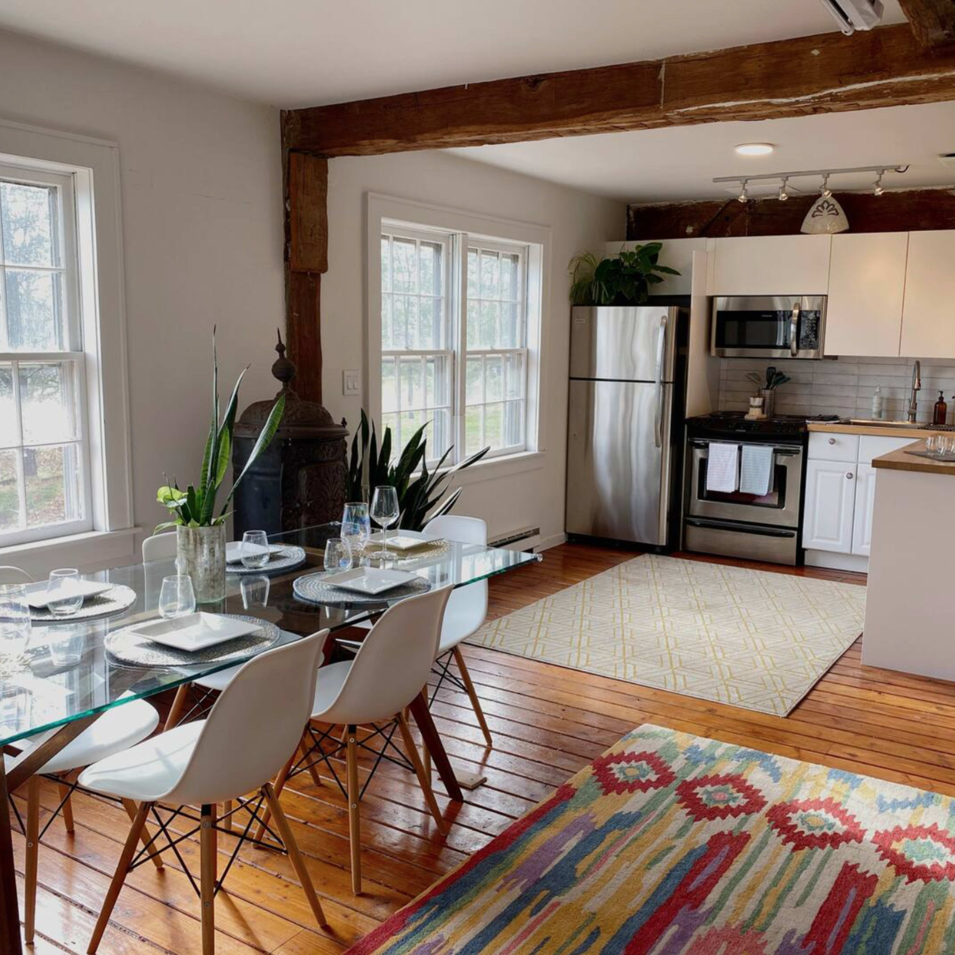 A modern kitchen and dining area with a glass dining table, white cabinets, stainless steel appliances, and wooden flooring.
