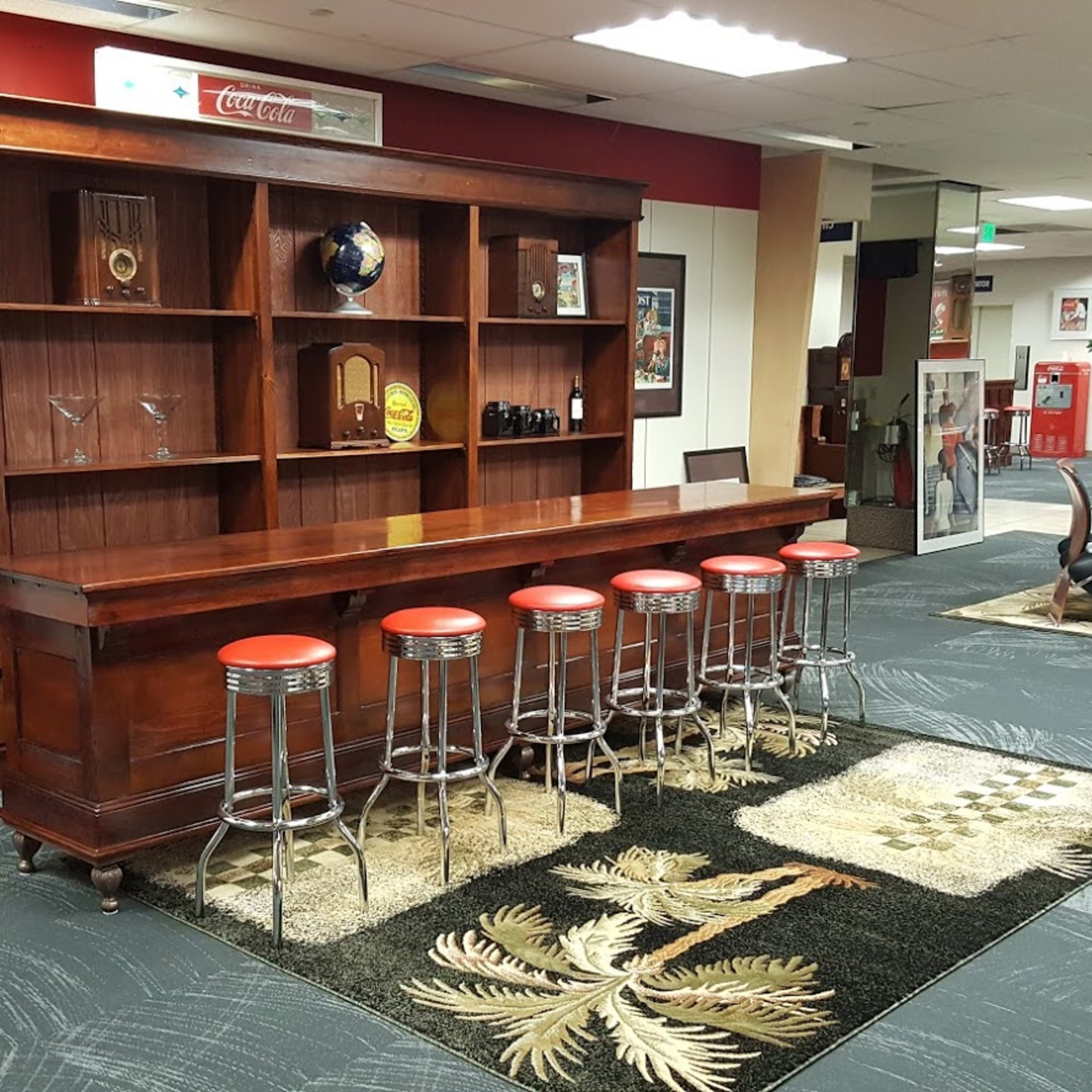 A wooden bar with red stools in front of a shelf filled with decorative items and a carpet featuring a leaf design.
