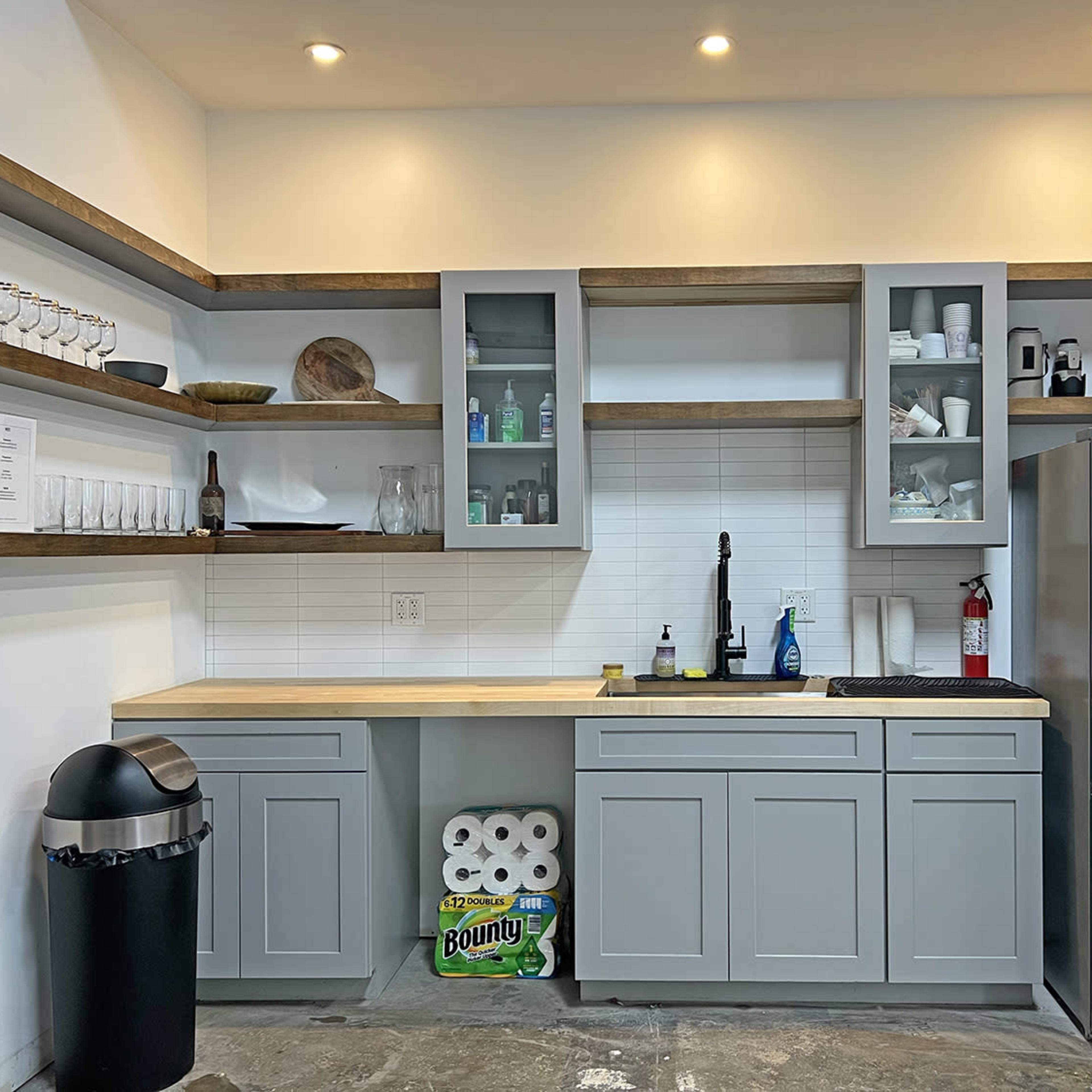 A modern kitchen with gray cabinets, a stainless steel refrigerator, and open shelving displaying various kitchen items.