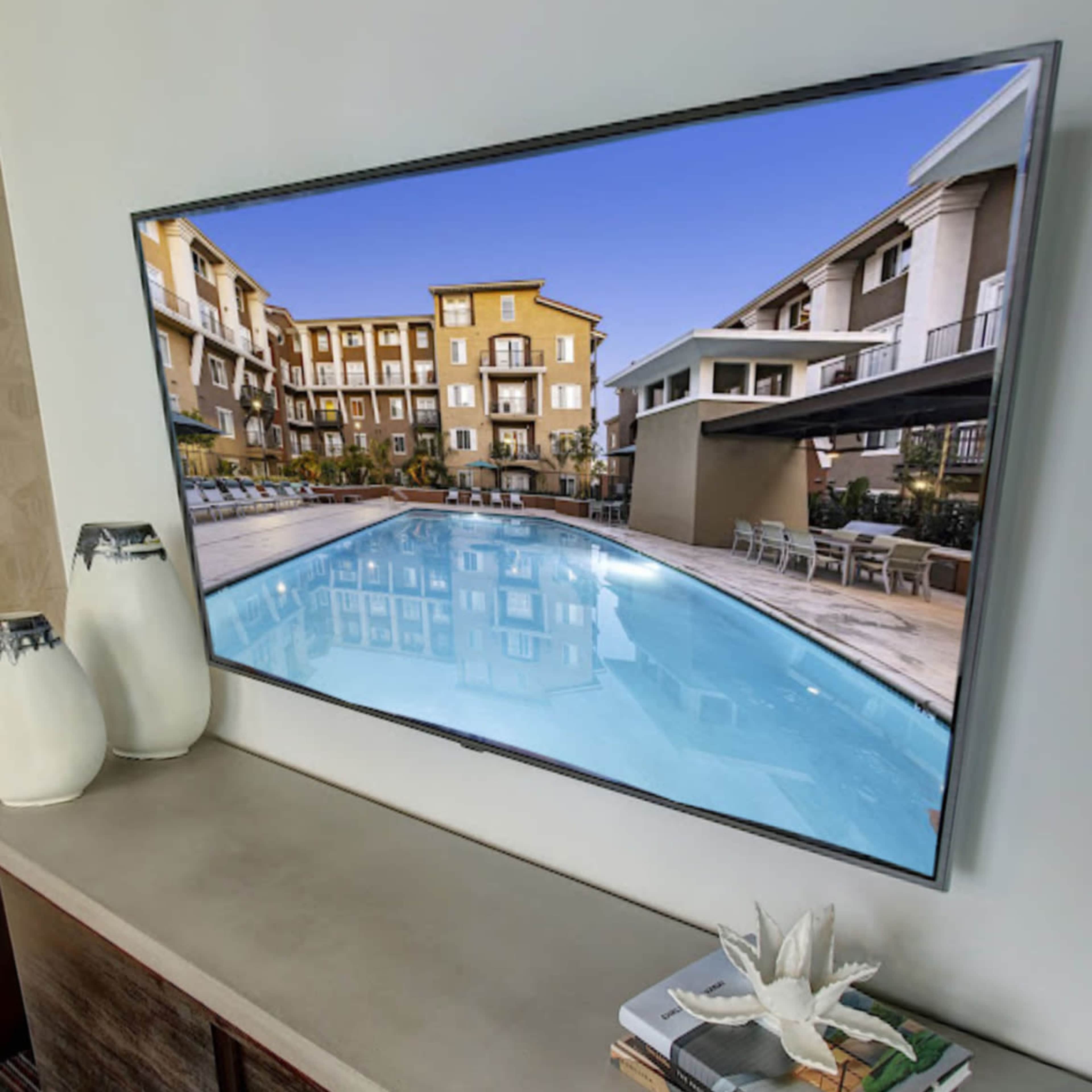A television displaying a swimming pool scene is mounted above a concrete countertop with decorative items and magazines.