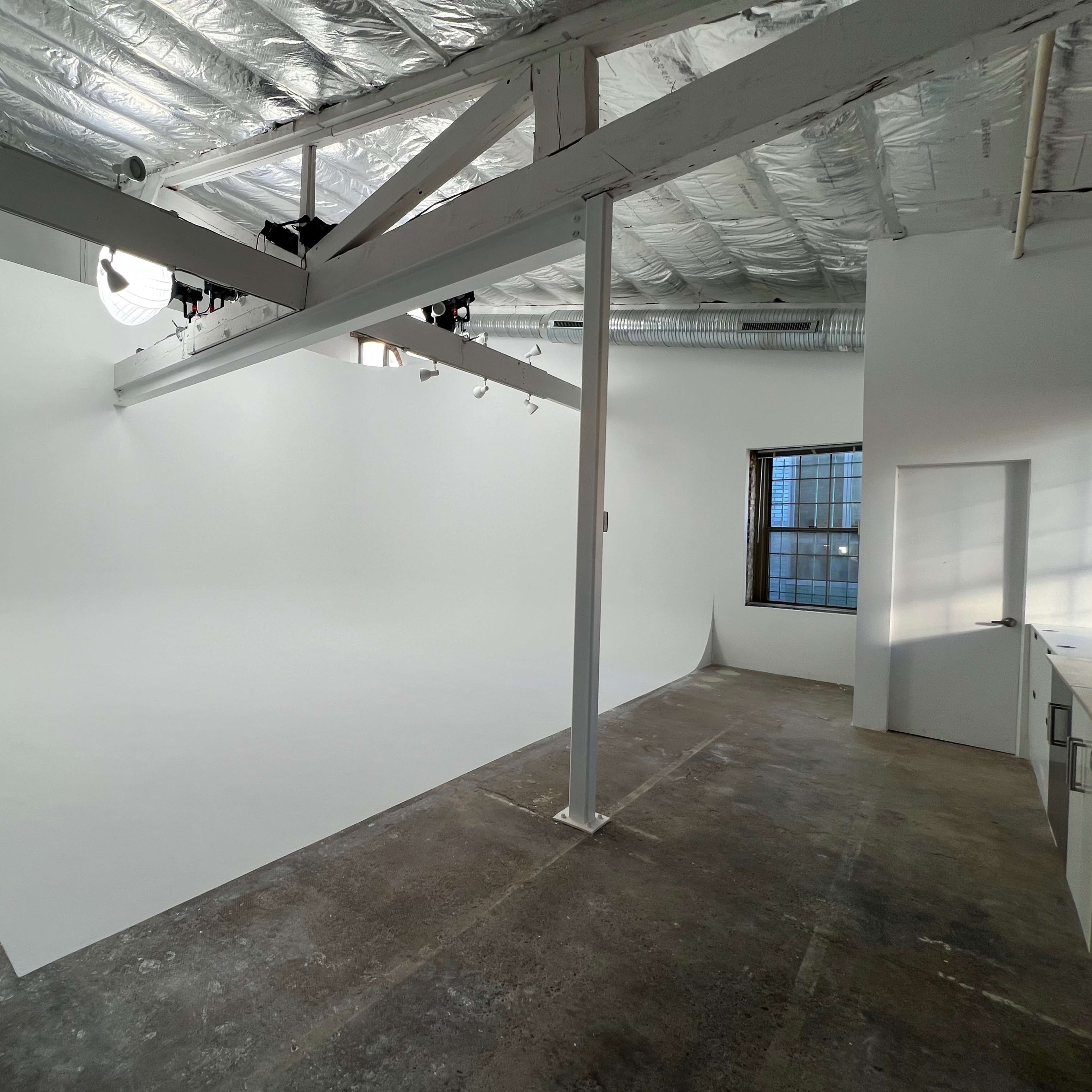 A spacious, empty studio with a curved white backdrop and large windows.