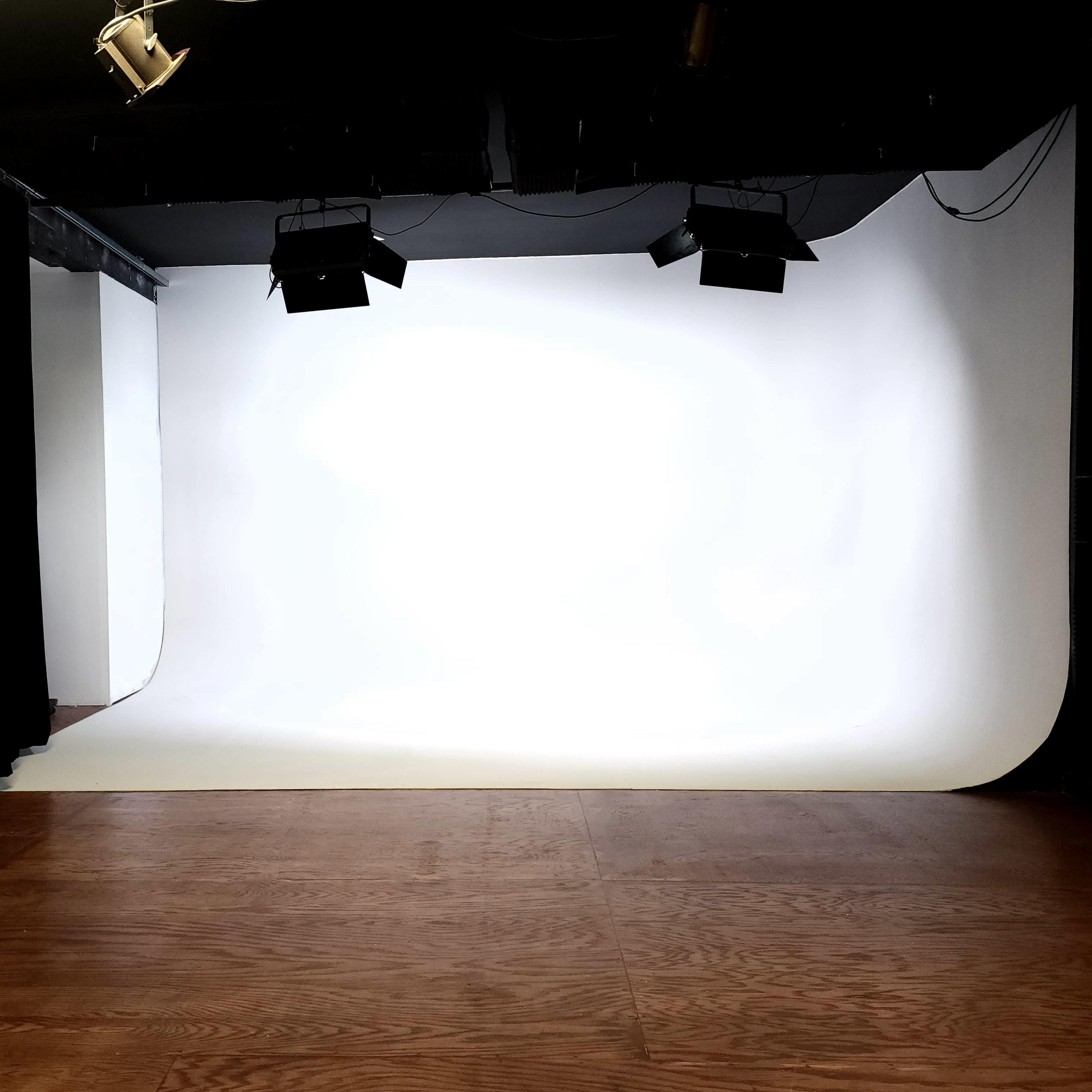 A photography studio features a seamless white backdrop with wooden flooring and black curtains.