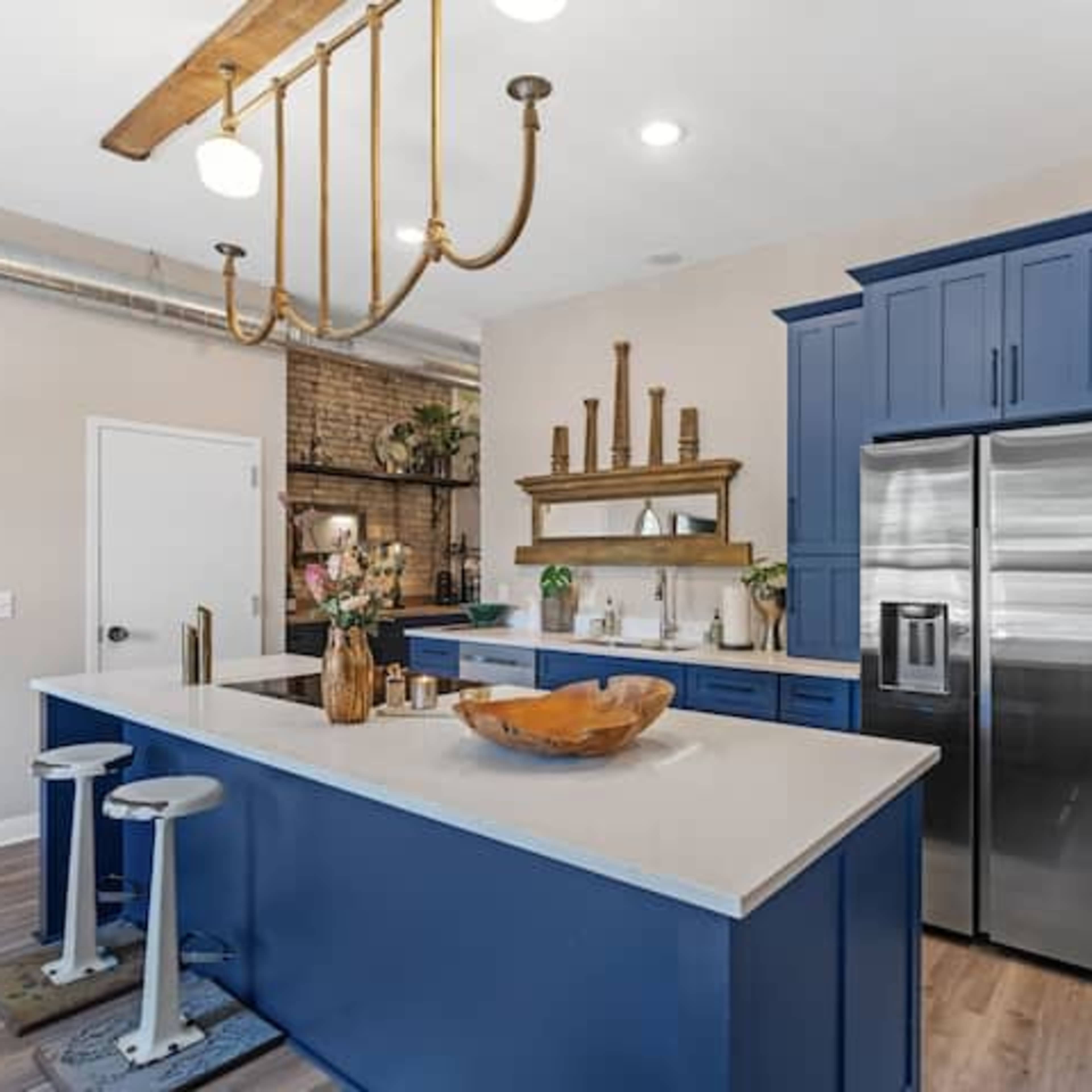 A modern kitchen features navy blue cabinetry, a large island with a wood bowl centerpiece, and stainless steel appliances.
