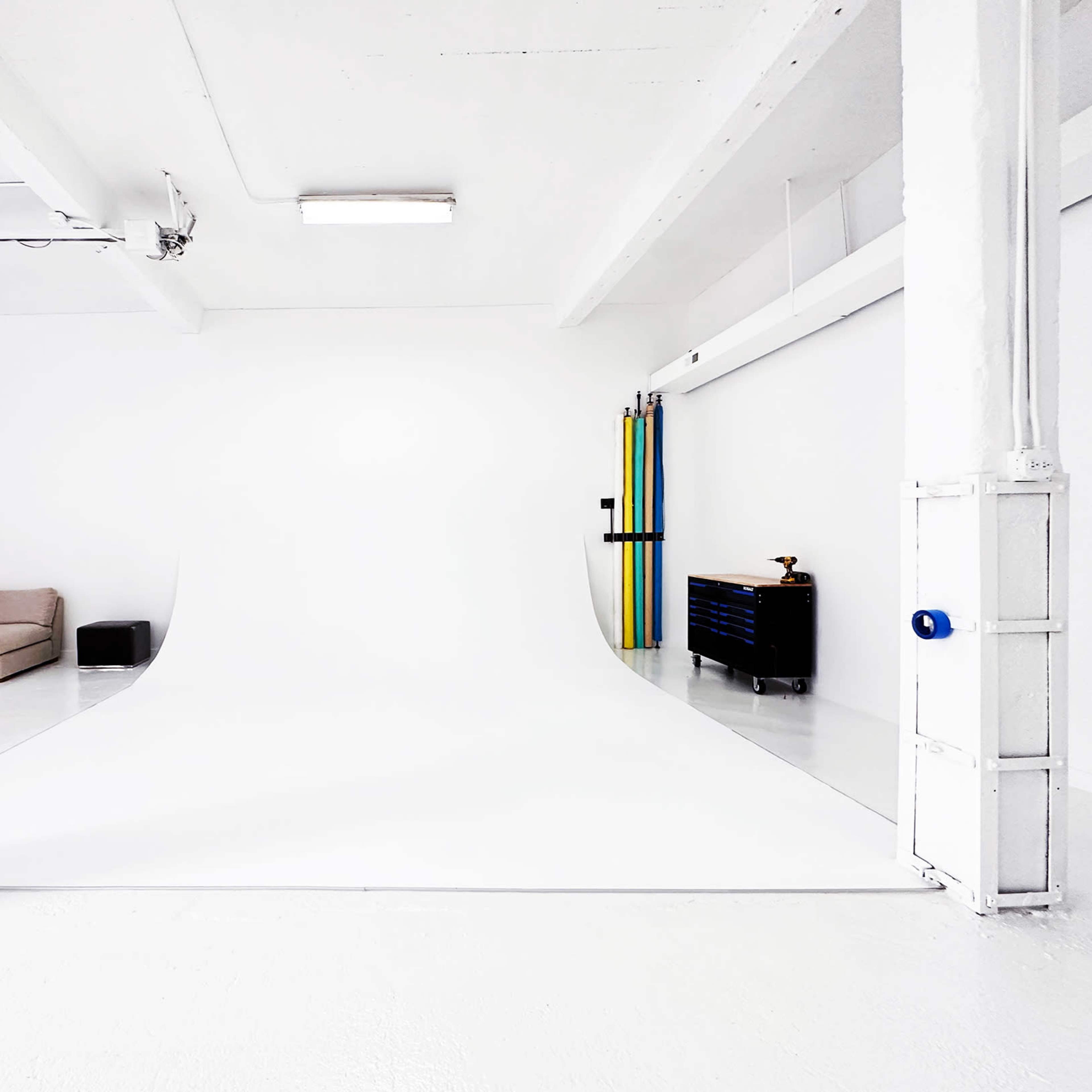 A spacious, minimalist studio with a white backdrop, a couch, a black storage box, and a tool chest against the wall.