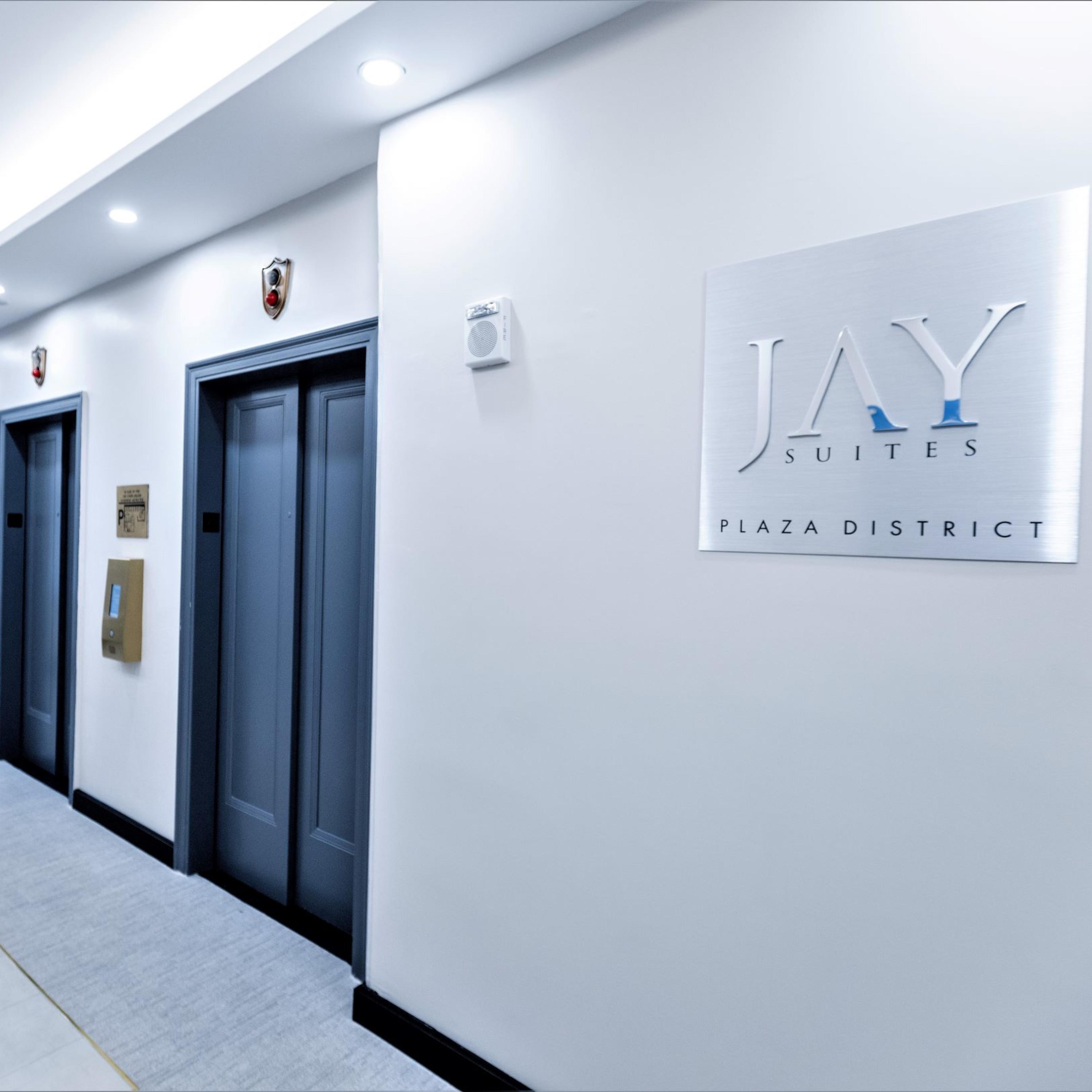 A modern hallway with elevator doors and a sign for Jay Suites in the Plaza District.