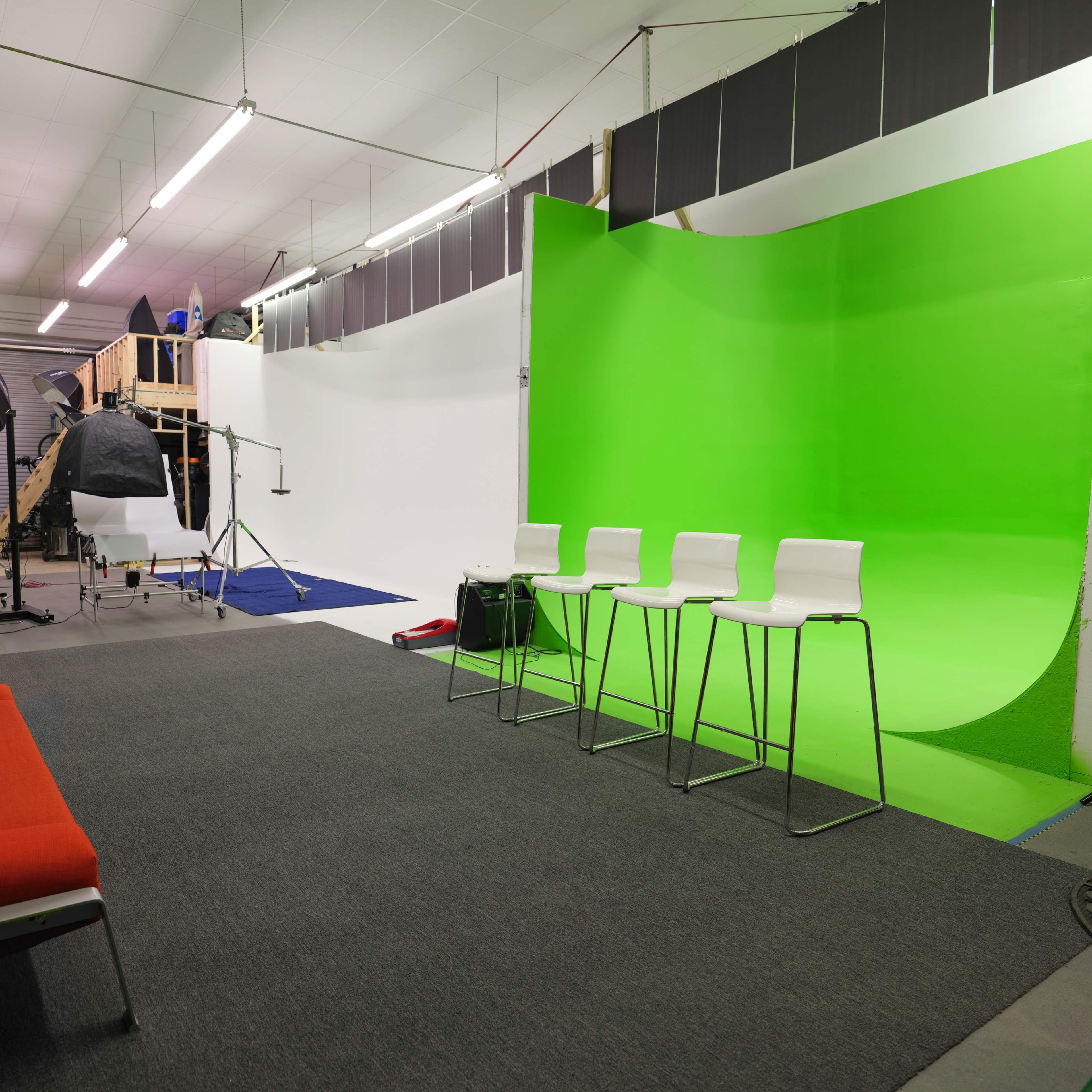 A photo studio with a green background, three white bar stools, and various photography equipment set up.