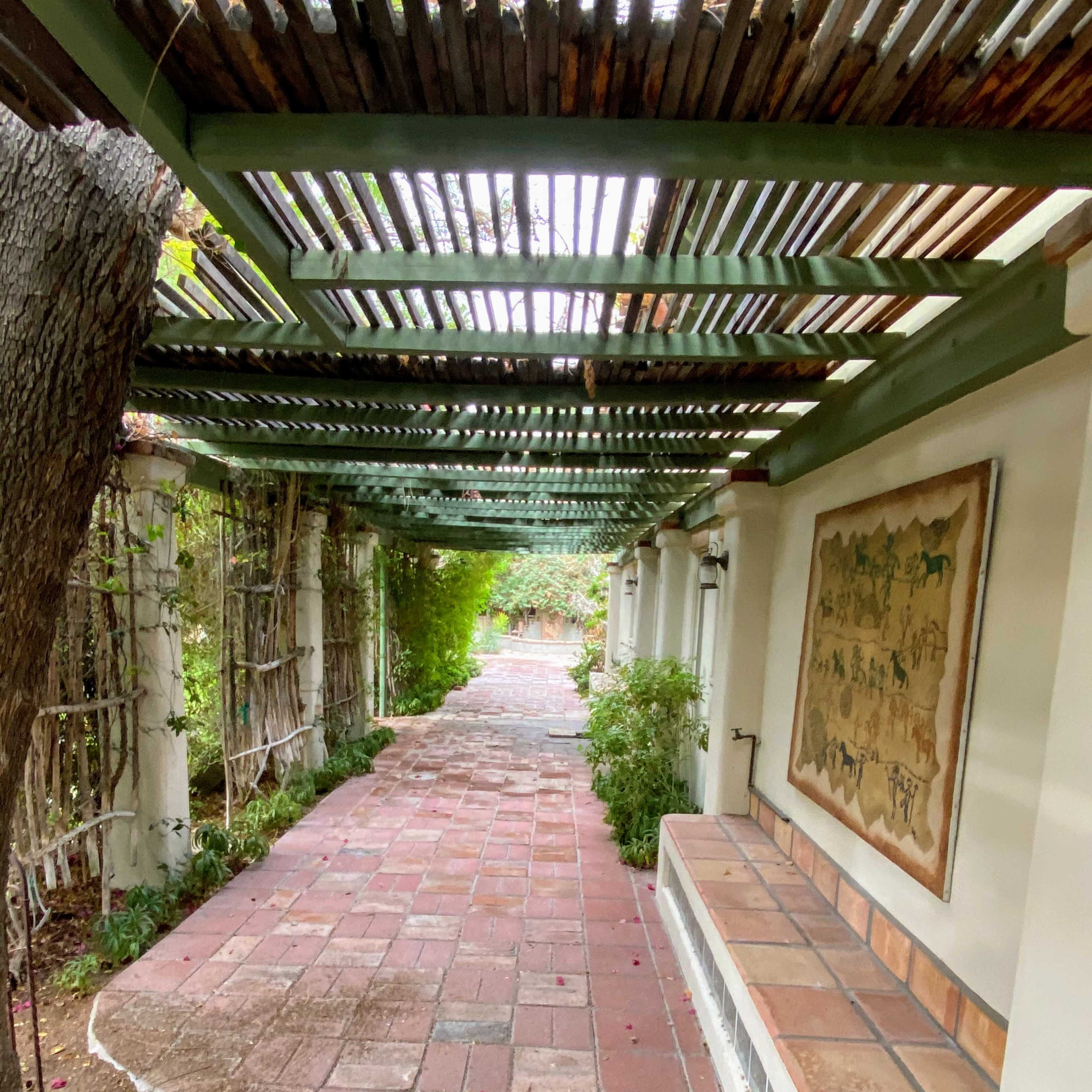 A paved walkway with a wooden lattice overhead leads through a landscaped garden.