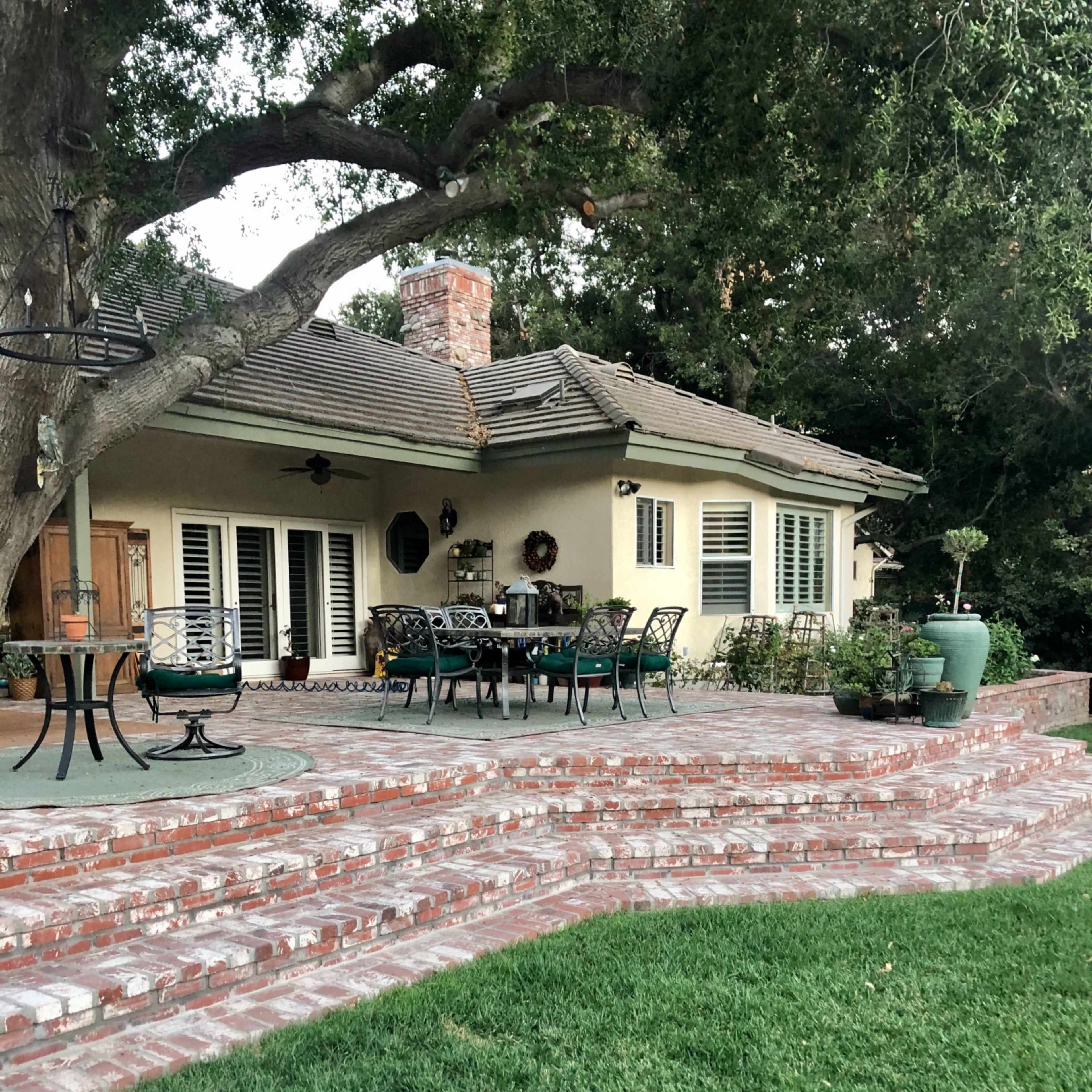A patio area with brick steps leading up to a house surrounded by greenery and outdoor furniture.