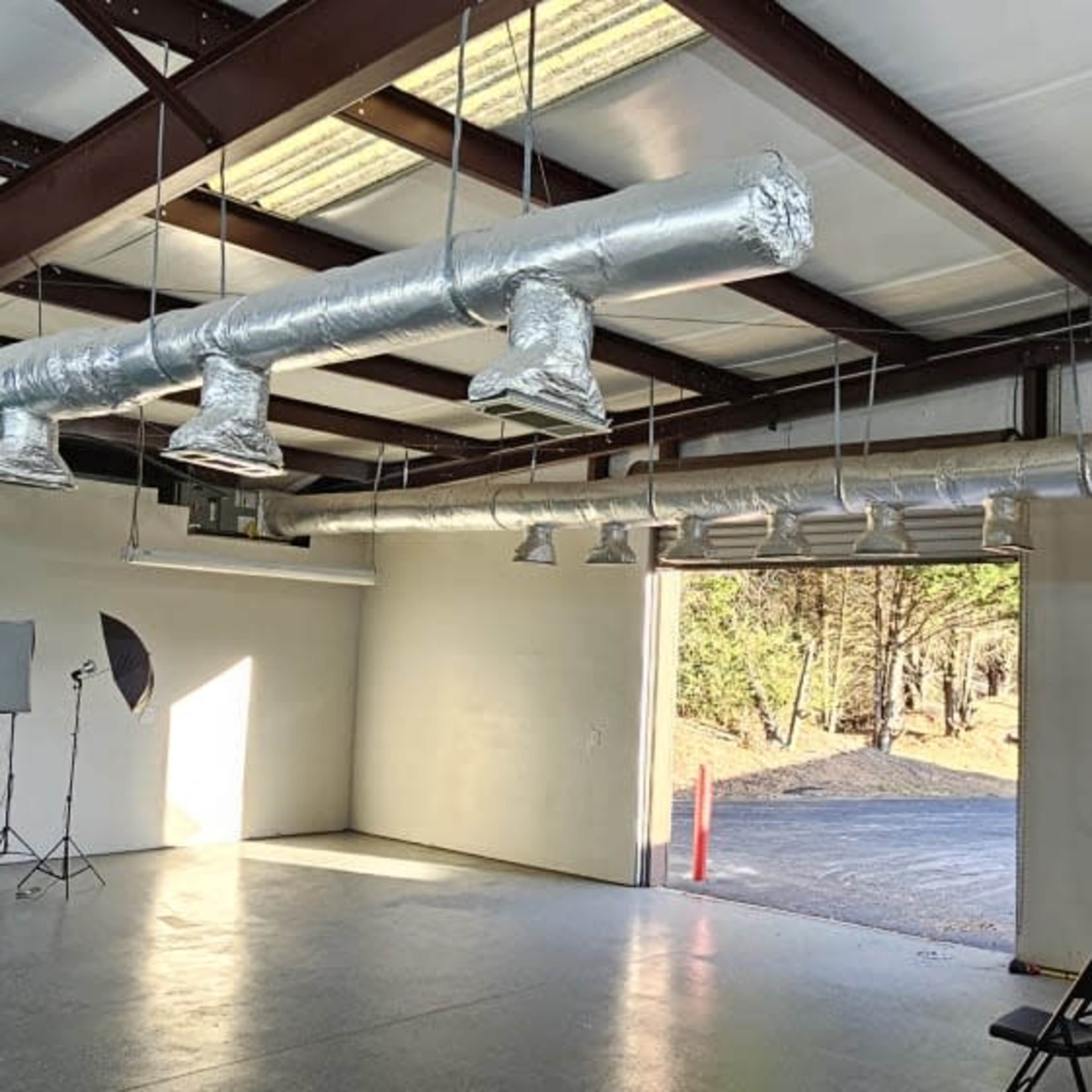 An empty industrial-style room with metal beams, ventilation ducts, and a green backdrop set against a wall.