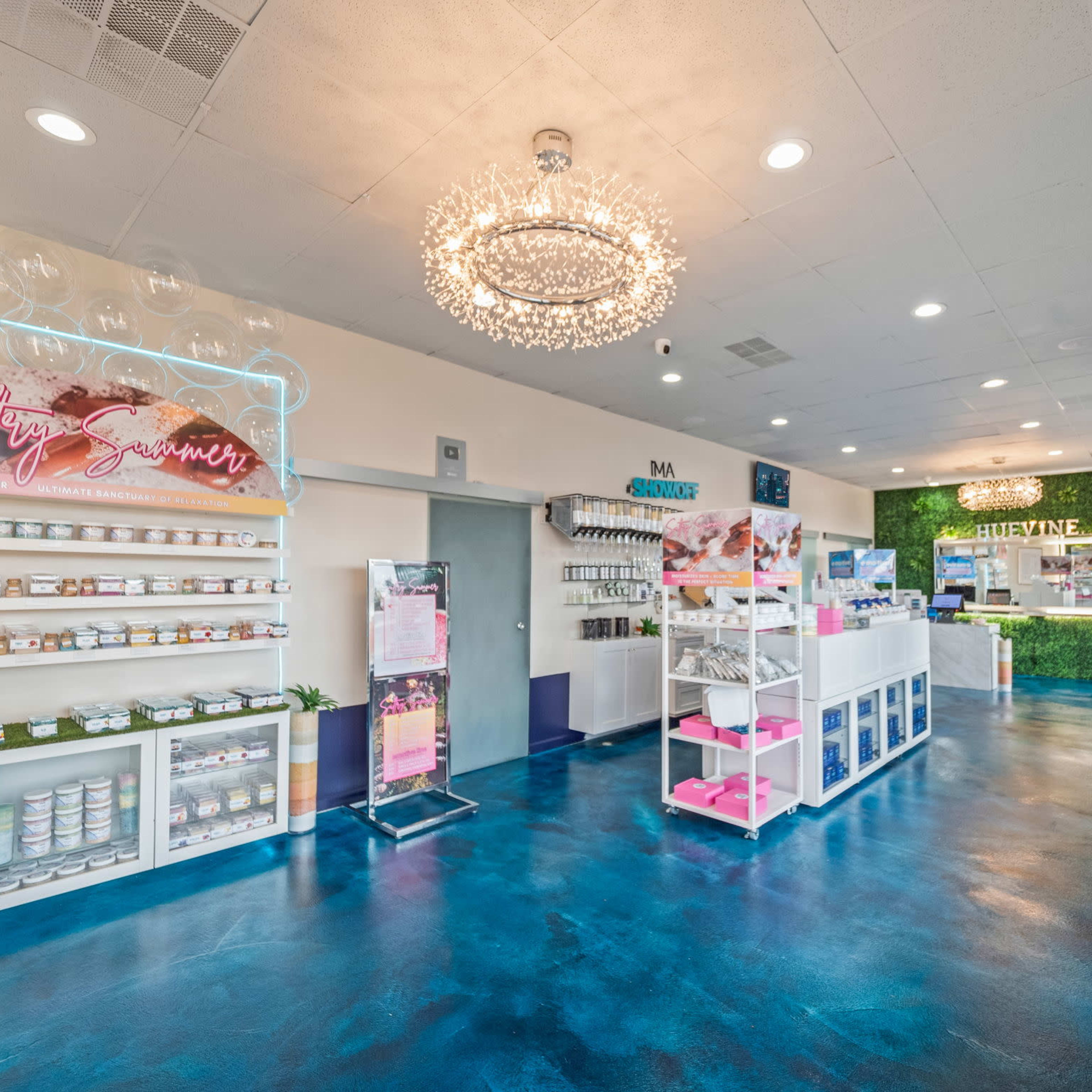 A brightly lit spa interior with a modern design featuring shelves of products, a reception desk, and greenery accents on the walls.